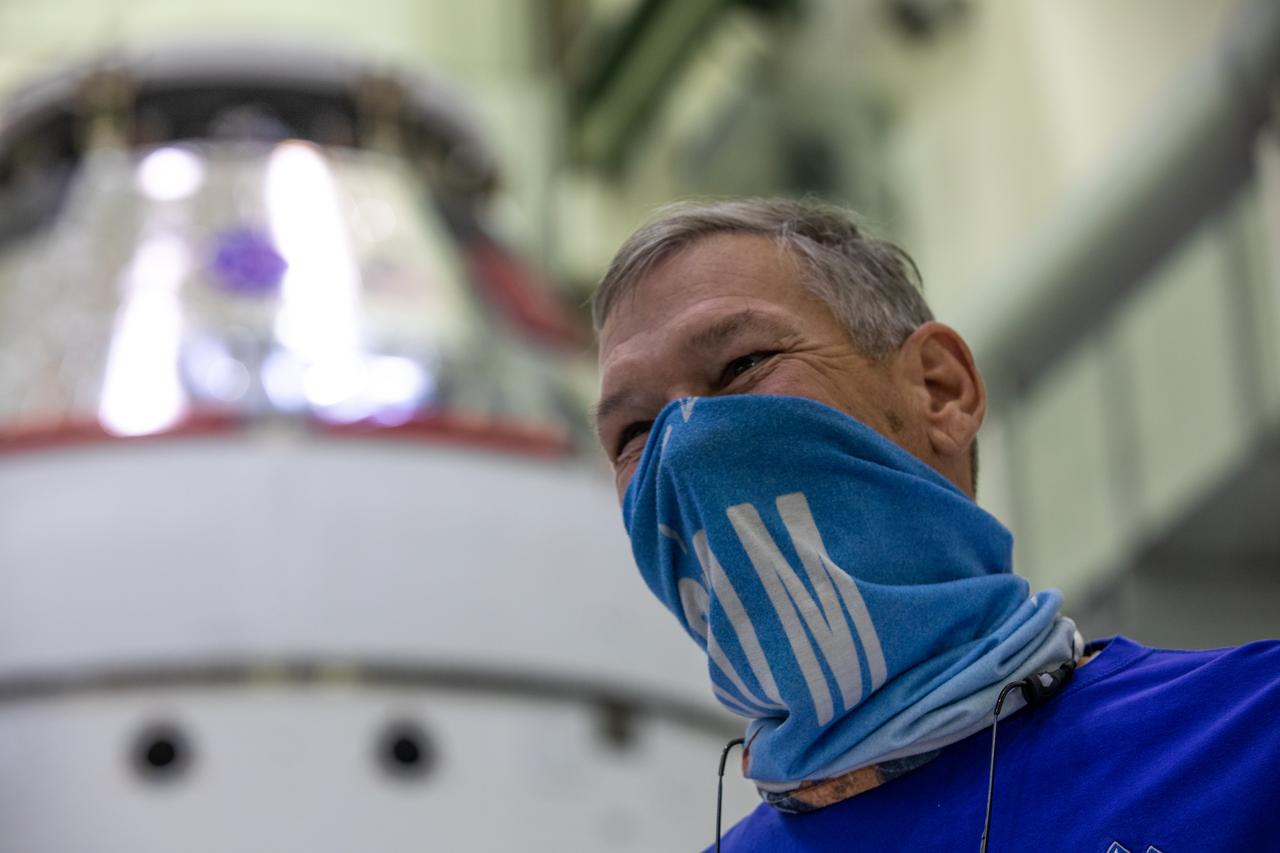 Todd Biddle, ASRC technician, is shown in the foreground with the Orion spacecraft for the Artemis I mission behind him inside the Neil Armstrong Operations and Checkout Building at NASA’s Kennedy Space Center in Florida on Oct. 28, 2020. The NASA insignia, also called the “meatball,” and American Fag have been applied to the Orion crew module back shell. Attached below Orion are the crew module adapter and the European Service Module (ESM) with spacecraft adapter jettison fairings installed. Recently, teams from across the globe installed the four solar array wings, which are housed inside the protective covering of the fairings. The fairing panels will encapsulate the ESM to protect it from harsh environments such as heat, wind, and acoustics as the spacecraft is propelled out of Earth’s atmosphere atop the Space Launch System rocket during NASA’s Artemis I mission.