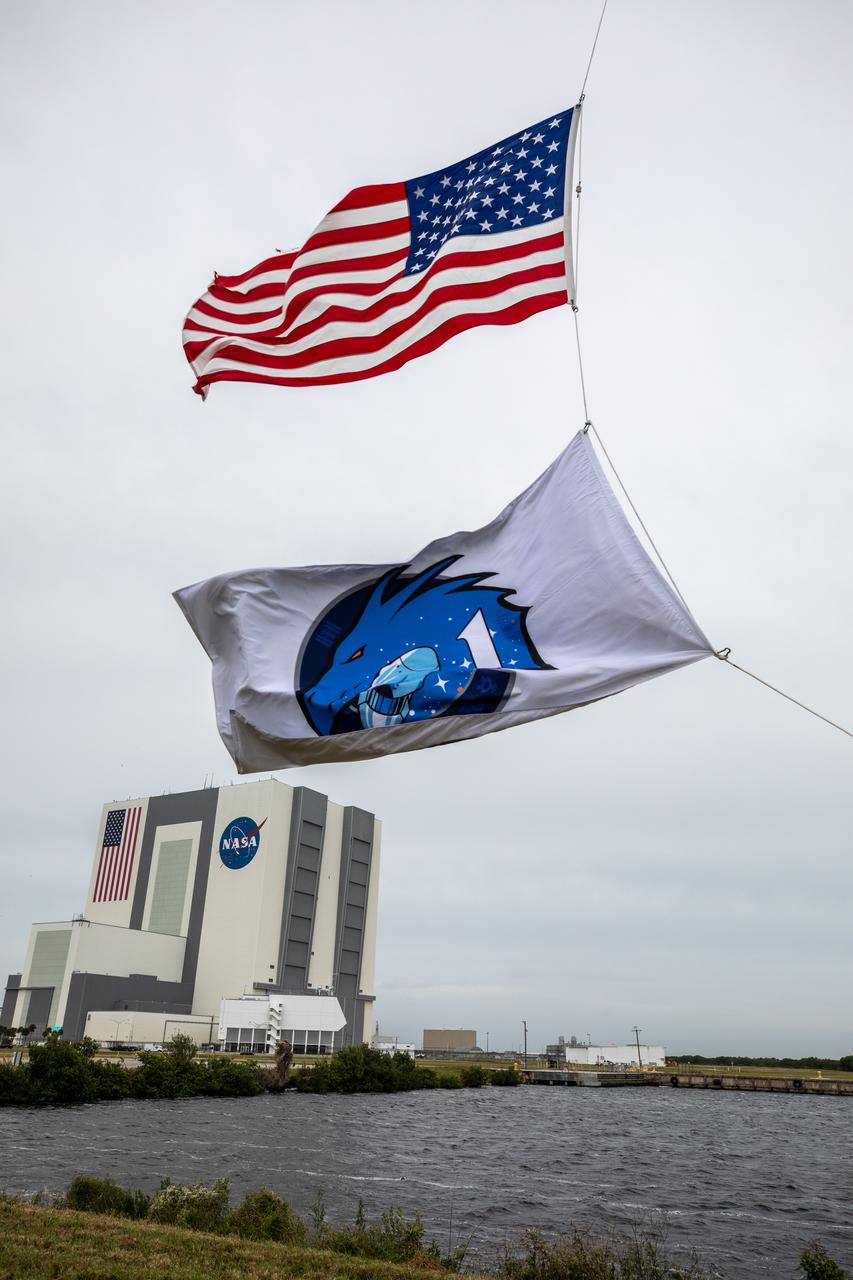 NASA’s SpaceX Crew-1 flag is raised beneath the American Flag near the countdown clock at the News Center at NASA’s Kennedy Space Center in Florida on Nov. 8, 2020. Crew-1 is the first regular crew mission of a U.S. commercial spacecraft with astronauts to the International Space Station as part of NASA’s Commercial Crew Program. The SpaceX Crew Dragon Resilience capsule will launch atop the company’s Falcon 9 rocket from Launch Complex 39A with NASA astronaut Michael Hopkins, spacecraft commander; NASA astronaut Victor Glover, pilot; NASA astronaut Shannon Walker, mission specialist; and JAXA astronaut Soichi Noguchi, mission specialist, to the space station for a six-month science mission.