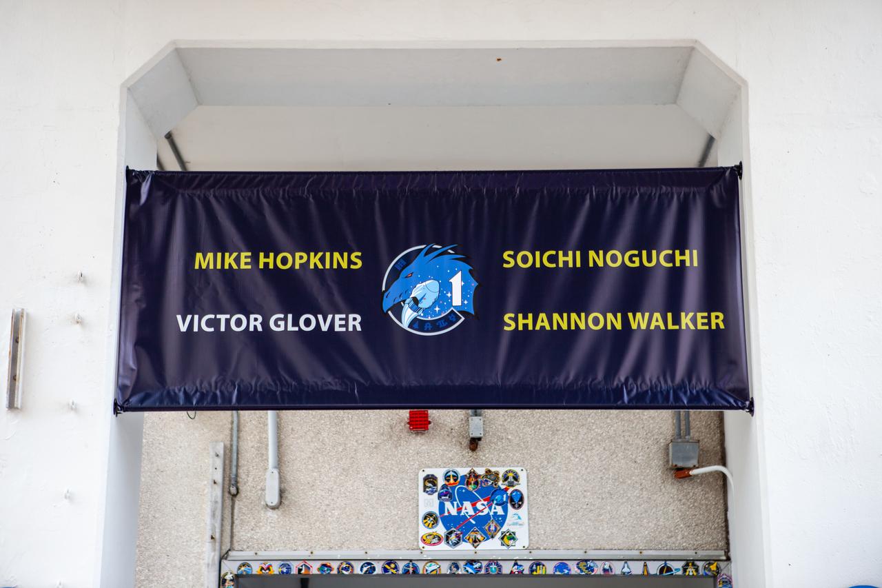 A banner hangs above the door where NASA SpaceX’s Crew-1 astronauts will exit from at the Neil Armstrong Operations and Checkout Building at NASA’s Kennedy Space Center in Florida on Nov. 15, 2020. NASA astronauts Michael Hopkins, Victor Glover and Shannon Walker, and JAXA astronaut Soichi Noguchi, will board two Tesla vehicles for the trip to Launch Complex 39A. Crew-1 is the first regular crew mission of a U.S. commercial spacecraft with astronauts to the International Space Station as part of NASA’s Commercial Crew Program. The SpaceX Crew Dragon Resilience capsule will launch atop the company’s Falcon 9 rocket from Pad 39A to the space station for a six-month science mission.