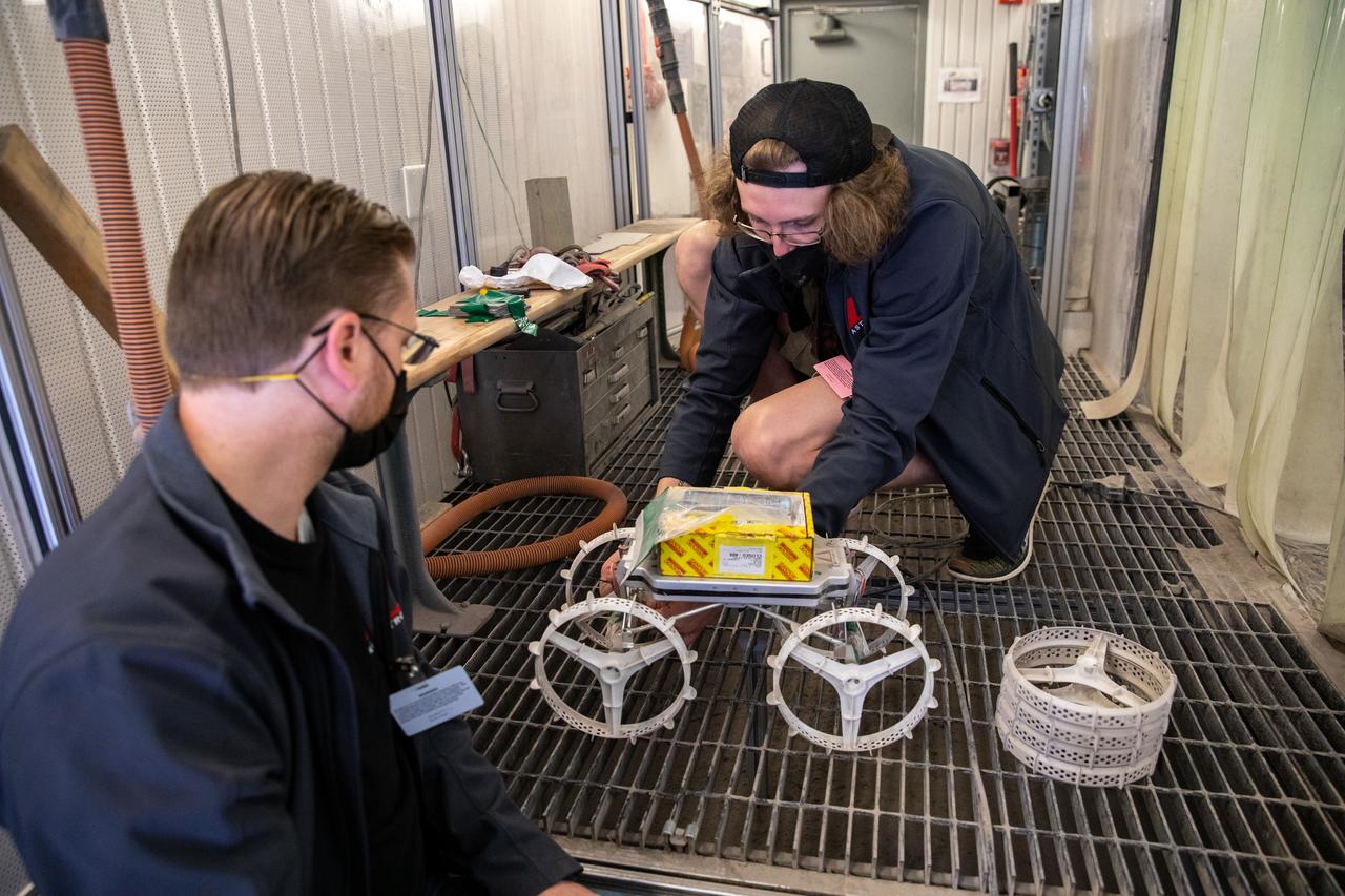 Astrobotic employees Troy Arbuckle, at left, Planetary Mobility lead mechanical engineer, and Taylor Whitaker, flight software engineer, prepare the Astrobotic CubeRover for its test run in the Granular Mechanics and Regolith Operations Laboratory regolith bin at NASA’s Kennedy Space Center in Florida on Dec. 10, 2020. The regolith bin simulates the mechanical properties of the Moon’s surface. NASA and Astrobotic employees put the CubeRover through a series of more than 150 mobility tests over several days to evaluate and improve wheel design.