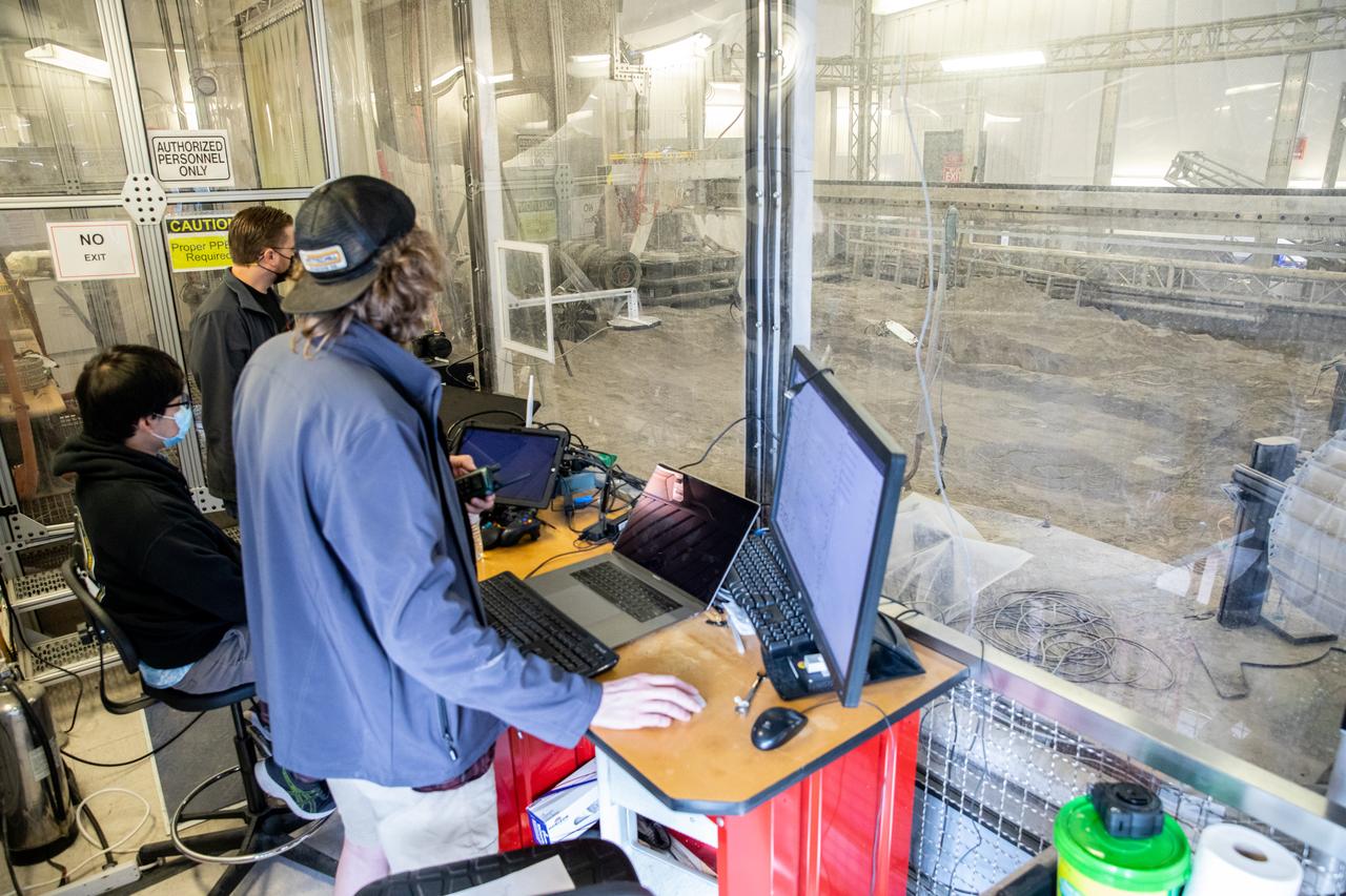 Astrobotic employees Troy Arbuckle, at far left, Planetary Mobility lead mechanical engineer; Takuto Oikawa, mechanical engineer; and Taylor Whitaker, flight software engineer, monitor the progress of the Astrobotic CubeRover during its test run in the Granular Mechanics and Regolith Operations Lab regolith at NASA’s Kennedy Space Center in Florida on Dec. 10, 2020. The regolith bin simulates the mechanical properties of the Moon’s surface. NASA and Astrobotic employees put the CubeRover through a series of more than 150 mobility tests over several days to evaluate and improve wheel design.