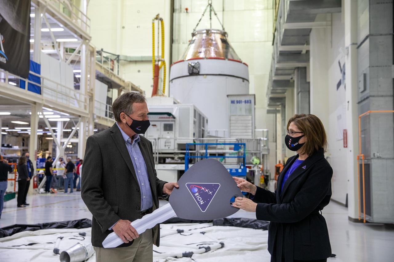 Orion is revealed for one of the final times on Jan. 14, as it is readied atop its transport pallet from the Neil Armstrong Operations and Checkout Building at NASA’s Kennedy Space Center in Florida, along its path to the pad ahead of the Artemis I launch. Mike Bolger, at left, manager of Exploration Ground Systems (EGS), receives the “key” to Orion from Cathy Koerner, Orion Program manager signifying the transfer of the spacecraft from the assembly to the ground system processing team. Teams across the globe have worked tirelessly to assemble the spacecraft, which will receive a protective covering prior to departing for the Multi-Payload Processing Facility to begin ground processing by the EGS and Jacobs teams.