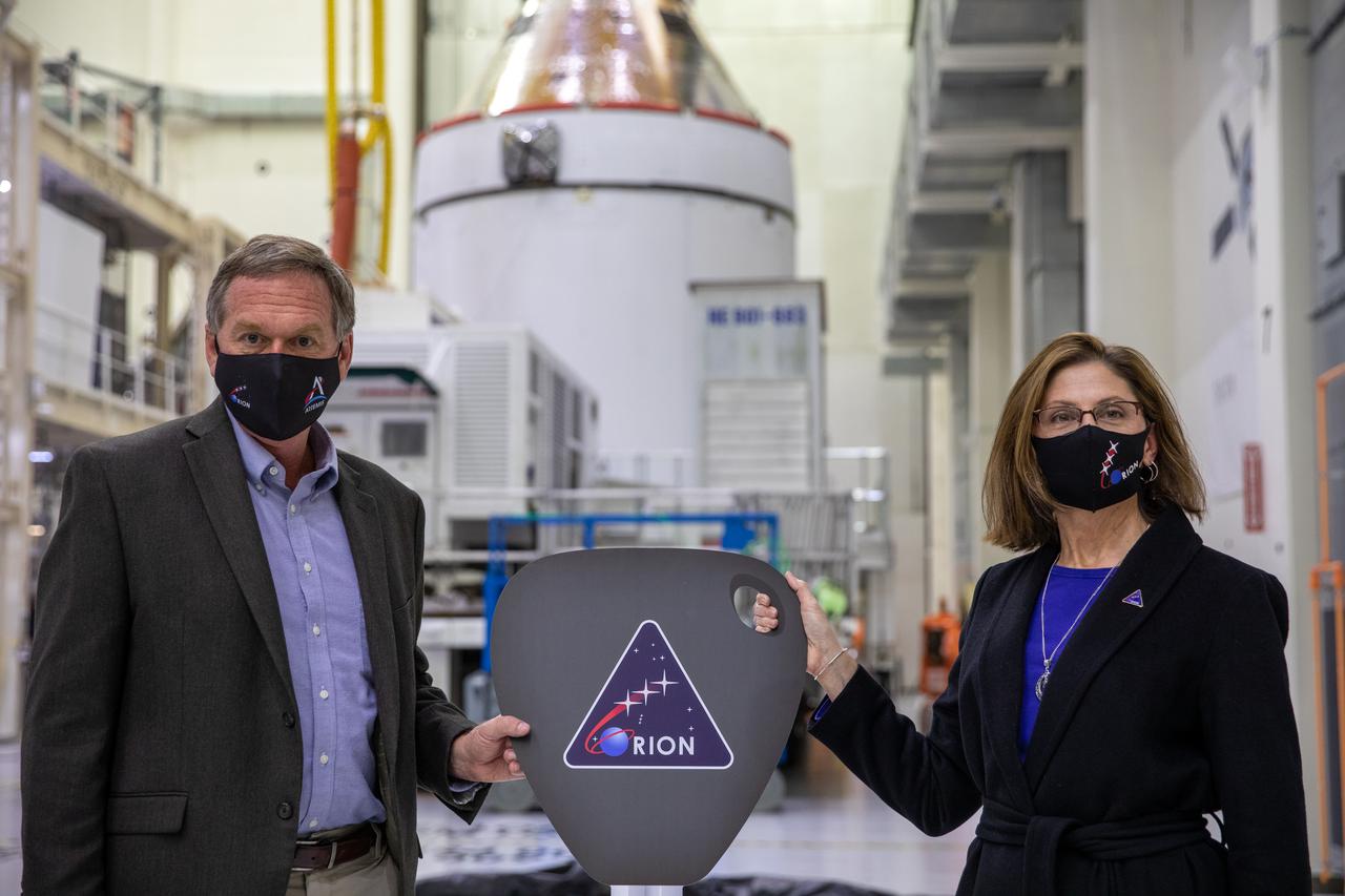 Orion is revealed for one of the final times on Jan. 14, as it is readied atop its transport pallet from the Neil Armstrong Operations and Checkout Building at NASA’s Kennedy Space Center in Florida, along its path to the pad ahead of the Artemis I launch. Mike Bolger, at left, manager of Exploration Ground Systems (EGS), receives the “key” to Orion from Cathy Koerner, Orion Program manager, signifying the transfer of the spacecraft from the assembly to the ground system processing team. Teams across the globe have worked tirelessly to assemble the spacecraft, which will receive a protective covering prior to departing for the Multi-Payload Processing Facility to begin ground processing by the EGS and Jacobs teams.