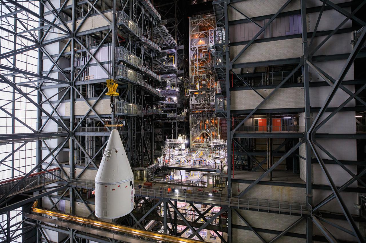 In the transfer aisle of the Vehicle Assembly Building at NASA’s Kennedy Space Center in Florida, workers use a crane to lift the right-hand forward assembly for the Space Launch System (SLS) high up for transfer into High Bay 3 on March 2, 2021. The forward assembly will be attached to the center forward segment on the mobile launcher (ML). Workers with Exploration Ground Systems and contractor Jacobs teams are stacking the twin five-segment boosters on the ML over a number of weeks. When the core stage arrives, it will join the boosters on the mobile launcher, followed by the interim cryogenic propulsion stage and Orion spacecraft. Manufactured by Northrop Grumman in Utah, the twin boosters provide more than 75 percent of the total SLS thrust at launch. Marshall Space Flight Center in Huntsville, Alabama, manages the SLS. Under the Artemis program, NASA will land the first woman and the next man on the Moon. The first in a series of increasingly complex missions, Artemis I will test the Orion spacecraft and SLS as an integrated system ahead of crewed flights to the Moon.