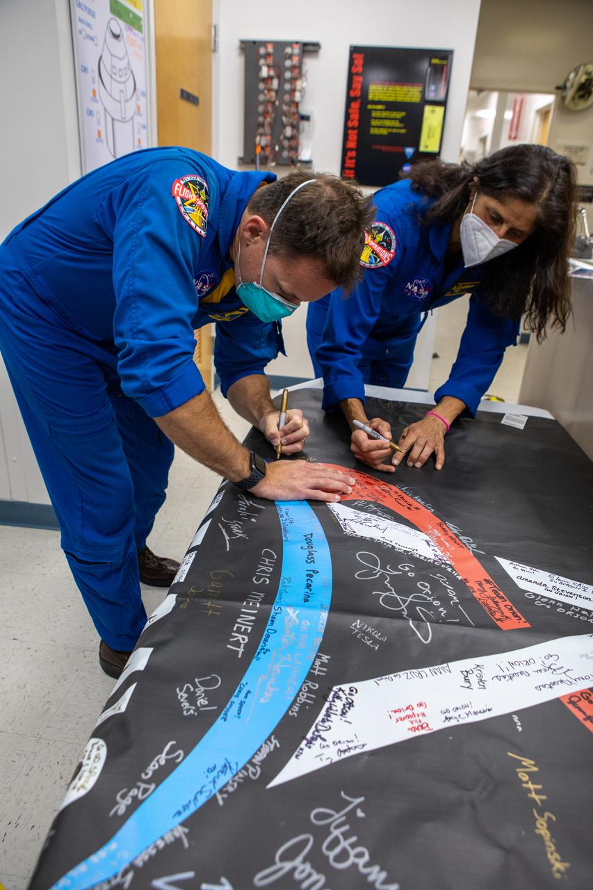 NASA astronauts Josh Cassada, left, and Sunita “Suni” Williams add their signatures to an Artemis “We Are Going” banner inside the Multi-Payload Processing Facility (MPPF) during a visit to NASA’s Kennedy Space Center in Florida on April 6, 2021. During their time at Kennedy, they also had the opportunity to view the Orion spacecraft and Space Launch System’s (SLS) Interim Cryogenic Propulsion Stage – both being serviced inside the MPPF ahead of the Artemis I launch. The first in a series of increasingly complex missions, Artemis I will test Orion and SLS as an integrated system prior to crewed flights to the Moon.