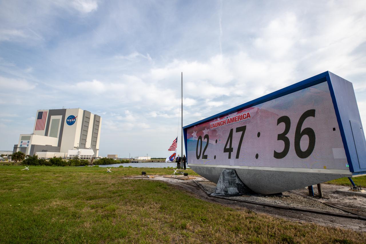 NASA acting administrator Steve Jurczyk raises the Crew-2 flag near the countdown clock at Kennedy Space Center’s Press Site on April 24, 2021. In the background is the Florida spaceport’s Vehicle Assembly Building. NASA’s SpaceX Crew-2 mission launched NASA astronaut Shane Kimbrough, spacecraft commander; NASA astronaut Megan McArthur, pilot; ESA astronaut Thomas Pesquet, mission specialist; and JAXA astronaut Akihiko Hoshide, mission specialist, to the International Space Station on April 23. Liftoff, from Kennedy’s Launch Complex 39A, was at 5:49 a.m. EDT. The SpaceX Crew Dragon Endeavour docked to the space station on April 24, at 5:08 a.m. EDT.