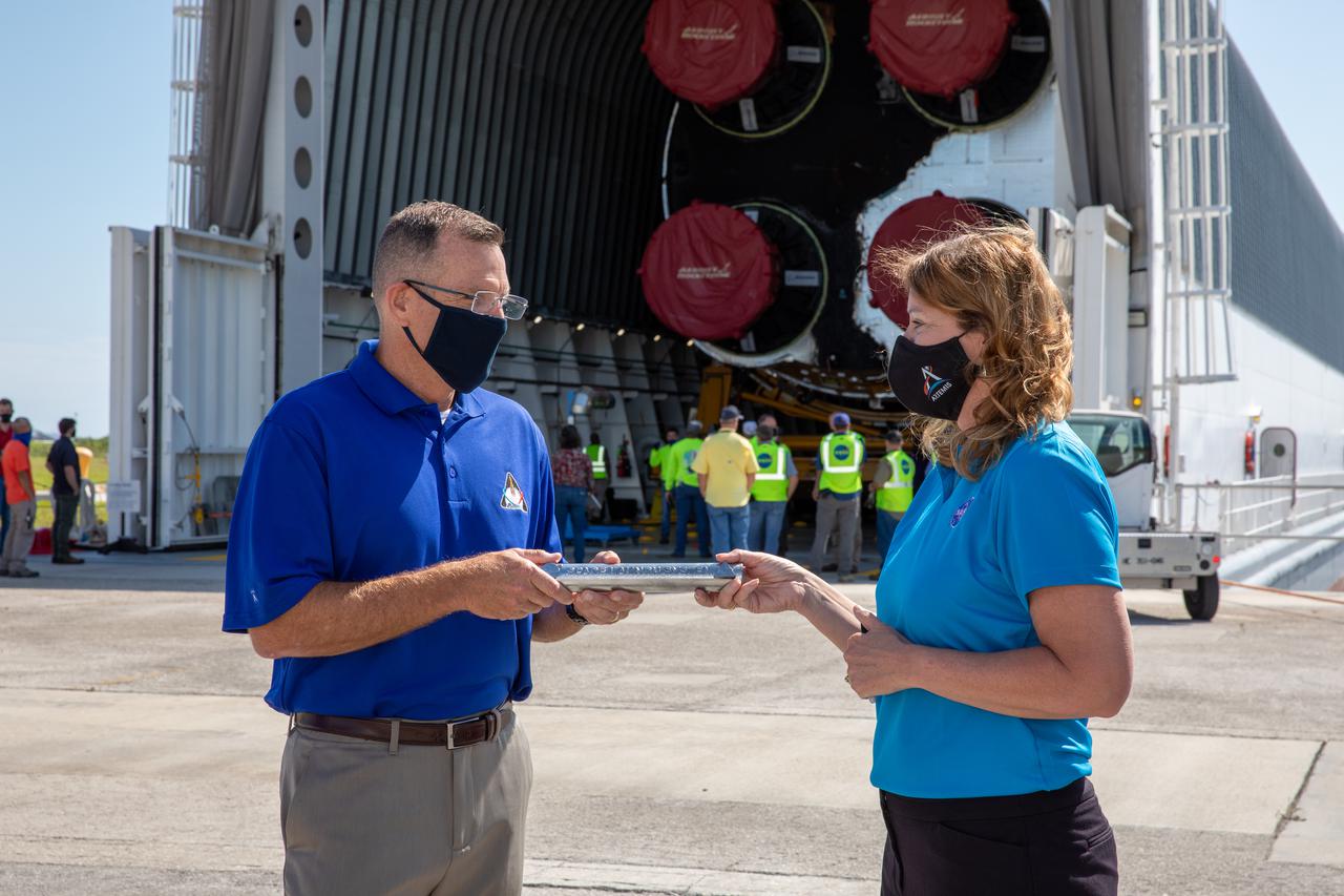 Space Launch System (SLS) Stages Manager Julie Bassler, right, celebrates the arrival of the SLS core stage by symbolically “passing the baton” to Exploration Ground Systems’ (EGS) Senior Vehicle Operations Manager Cliff Lanham on April 28, 2021, at NASA’s Kennedy Space Center in Florida. Journeying from the agency’s Stennis Space Center in Mississippi aboard the Pegasus barge, the core stage arrived at the Florida spaceport on April 27 to be processed for flight by EGS. It is the final piece of Artemis hardware to arrive at Kennedy and will be offloaded and moved to the Vehicle Assembly Building, where it will be prepared for integration atop the mobile launcher with the completed stack of solid rocket boosters ahead of the Artemis I launch. The first in a series of increasingly complex missions, Artemis I will test SLS and Orion as an integrated system prior to crewed flights to the Moon.