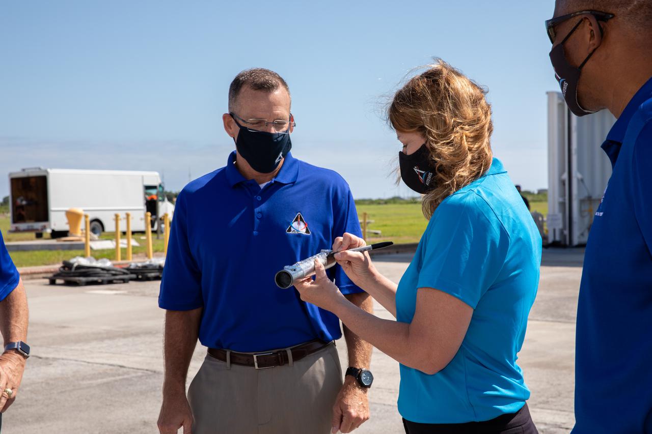 Space Launch System (SLS) Stages Manager Julie Bassler, right, celebrates the arrival of the SLS core stage by symbolically “passing the baton” to Exploration Ground Systems’ (EGS) Senior Vehicle Operations Manager Cliff Lanham on April 28, 2021, at NASA’s Kennedy Space Center in Florida. Journeying from the agency’s Stennis Space Center in Mississippi aboard the Pegasus barge, the core stage arrived at the Florida spaceport on April 27 to be processed for flight by EGS. It is the final piece of Artemis hardware to arrive at Kennedy and will be offloaded and moved to the Vehicle Assembly Building, where it will be prepared for integration atop the mobile launcher with the completed stack of solid rocket boosters ahead of the Artemis I launch. The first in a series of increasingly complex missions, Artemis I will test SLS and Orion as an integrated system prior to crewed flights to the Moon.