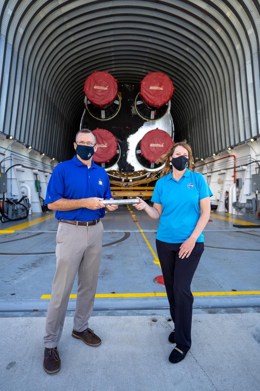 Space Launch System (SLS) Stages Manager Julie Bassler, right, celebrates the arrival of the SLS core stage by symbolically “passing the baton” to Exploration Ground Systems’ (EGS) Senior Vehicle Operations Manager Cliff Lanham on April 28, 2021, at NASA’s Kennedy Space Center in Florida. Journeying from the agency’s Stennis Space Center in Mississippi aboard the Pegasus barge, the core stage arrived at the Florida spaceport on April 27 to be processed for flight by EGS. It is the final piece of Artemis hardware to arrive at Kennedy and will be offloaded and moved to the Vehicle Assembly Building, where it will be prepared for integration atop the mobile launcher with the completed stack of solid rocket boosters ahead of the Artemis I launch. The first in a series of increasingly complex missions, Artemis I will test SLS and Orion as an integrated system prior to crewed flights to the Moon.