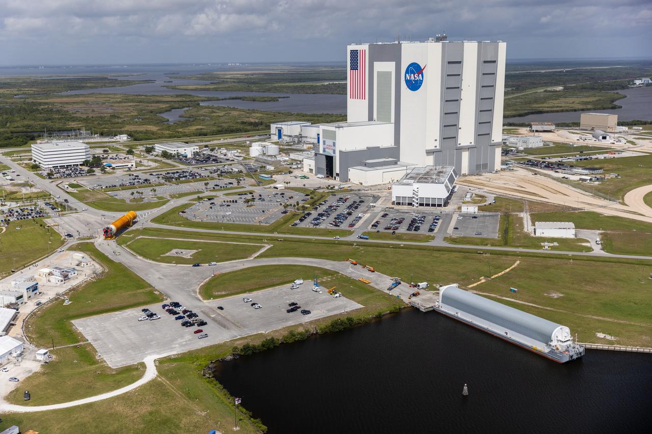 After completing its journey from NASA’s Stennis Space Center in Mississippi aboard the Pegasus barge, teams with Exploration Ground Systems (EGS) and lead contractor Jacobs transport the massive Space Launch System (SLS) core stage to Kennedy Space Center’s Vehicle Assembly Building in Florida on April 29, 2021 in this aerial view. Once inside the VAB, it will be prepared for integration with the completed stack of solid rocket boosters atop the mobile launcher ahead of the Artemis I launch. The first in a series of increasingly complex missions, Artemis I will test SLS and Orion as an integrated system prior to crewed flights to the Moon.