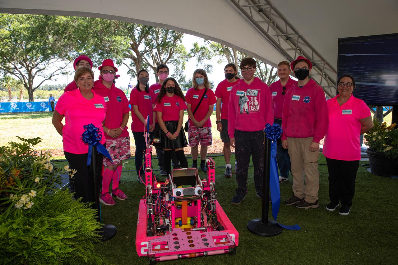 Students and faculty from Rockledge High School’s Pink Team, a robotics team mentored by NASA engineers, pose for a photo at NASA’s Kennedy Space Center Visitor Complex in Florida on June 11, 2021. Using the school’s 2021 competition robot – affectionately named “Pinky” – the Pink Team re-engineered their robot to carry a large pair of scissors to cut the ceremonial ribbon for the Florida Power and Light’s (FPL) Discovery Solar Energy Center becoming operational at the center. Discovery Solar Energy Center is a 74.5-megawatt solar site, spanning 491 acres at the spaceport. The site contains about 250,000 solar panels in total, producing enough energy to power approximately 15,000 homes. Harnessing energy from the Sun, the panels do not directly power anything at Kennedy, but rather, send energy directly to FPL's electricity grid for distribution to existing customers. Construction began in spring 2020, and the energy center became fully operational on May 30, 2021.