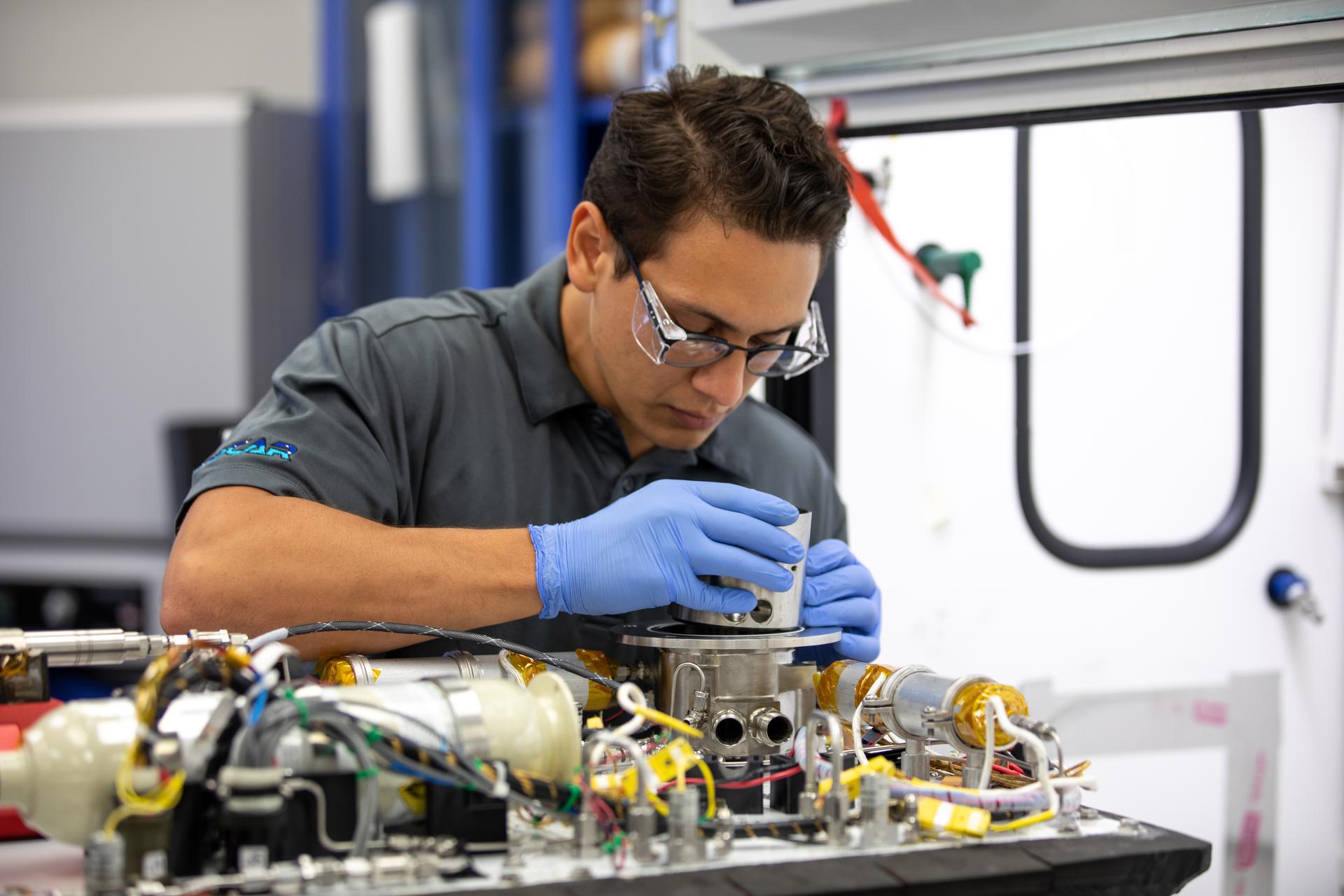 A researcher wearing safety glasses examines payload hardware in a lab.