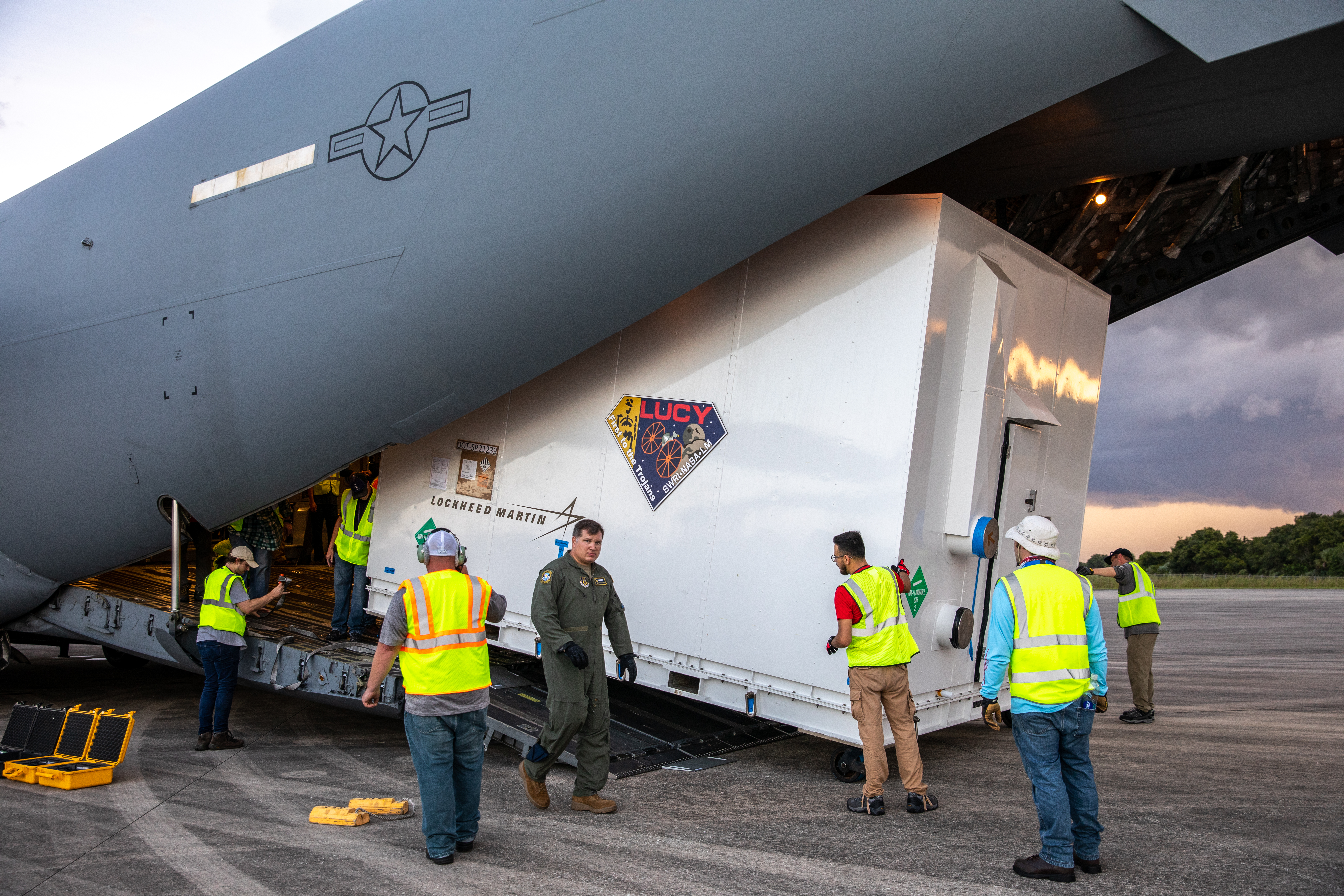 The shipping container holding NASA's Lucy spacecraft is unloaded from a United States Air Force C-17 cargo plane, stationed out of Charleston Air Force Base in South Carolina, on the runway of the Launch and Landing Facility at Kennedy Space Center in Florida on July 30, 2021. From there, the Lucy spacecraft will move to the Astrotech Space Operations payload processing facility in nearby Titusville, Florida, before its scheduled launch on a United Launch Alliance (ULA) Atlas V rocket from Cape Canaveral Space Force Station on October 16, 2021. The Lucy mission will be the first space mission to explore a diverse population of small bodies known as the Jupiter Trojan asteroids. The launch is being managed by NASA's Launch Services Program based at Kennedy, America's multi-user spaceport.