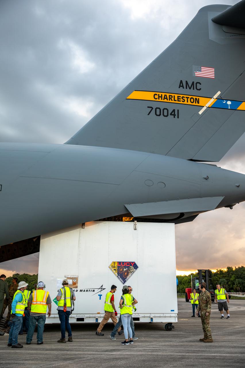 The shipping container holding NASA's Lucy spacecraft is unloaded from an Air Force C-17 cargo aircraft on the runway of the Launch and Landing Facility at Kennedy Space Center in Florida on July 30, 2021. From there, the Lucy spacecraft will move to the Astrotech Space Operations payload processing facility in nearby Titusville, Florida, before its scheduled launch on a United Launch Alliance (ULA) Atlas V rocket from Cape Canaveral Space Force Station on October 16, 2021. The Lucy mission will be the first space mission to explore a diverse population of small bodies known as the Jupiter Trojan asteroids. The launch is being managed by NASA's Launch Services Program based at Kennedy, America's premier multi-user spaceport. 