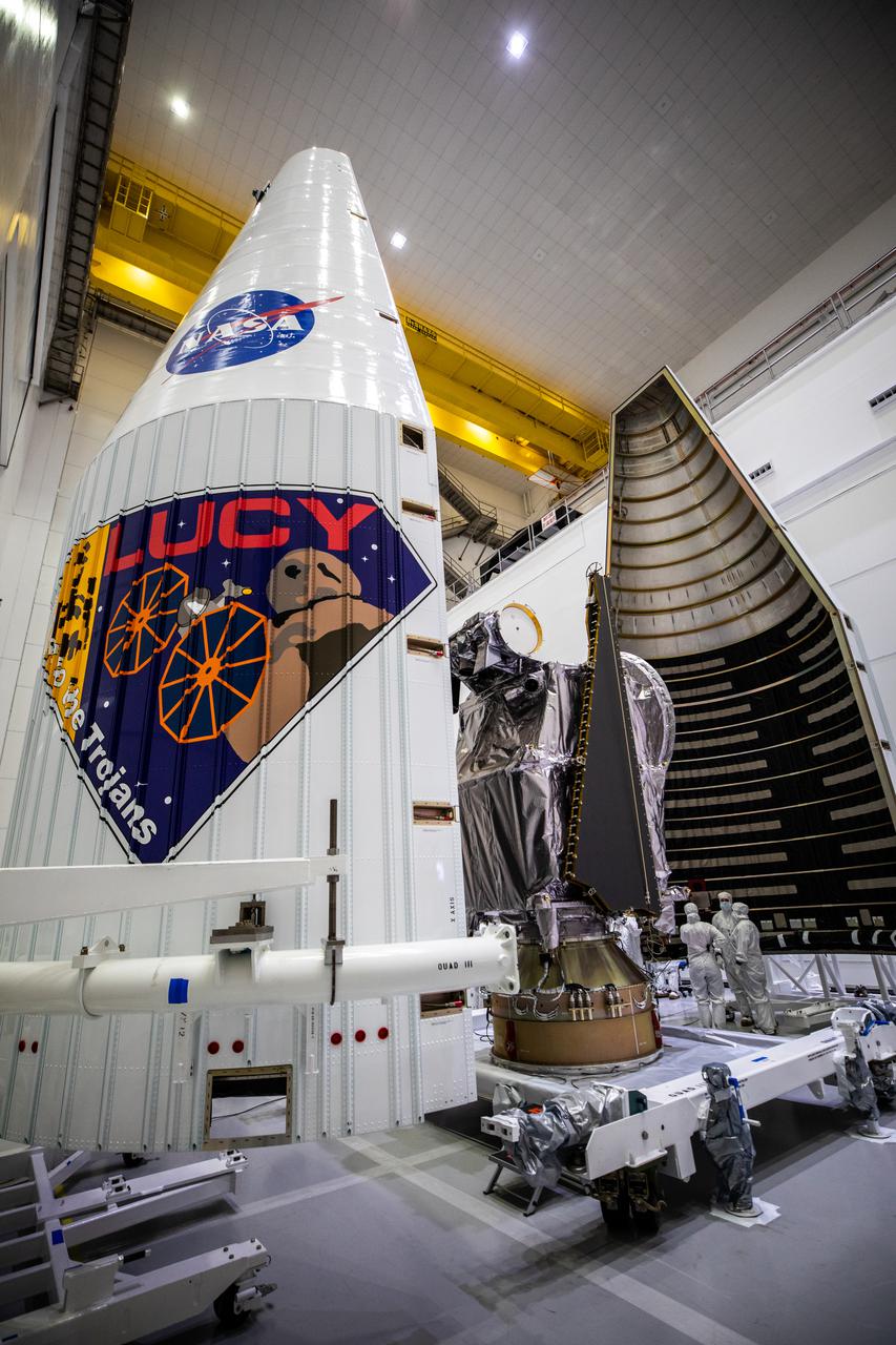 Workers inside the Astrotech Space Operations Facility in Titusville, Florida, move the first half of the United Launch Alliance (ULA) payload fairing toward NASA’s Lucy spacecraft on Sept. 30, 2021. The other half is in view in the foreground. The payload fairing will encapsulate and protect the spacecraft during launch and ascent. Lucy is scheduled to launch no earlier than Saturday, Oct. 16, on a ULA Atlas V 401 rocket from Space Launch Complex 41 at Cape Canaveral Space Force Station. NASA’s Launch Services Program based at Kennedy Space Center is managing the launch. Over its 12-year primary mission, Lucy will explore a record-breaking number of asteroids, flying by one asteroid in the solar system’s main belt and seven Trojan asteroids. Additionally, Lucy’s path will circle back to Earth three times for gravity assists, making it the first spacecraft ever to return to the vicinity of Earth from the outer solar system. 