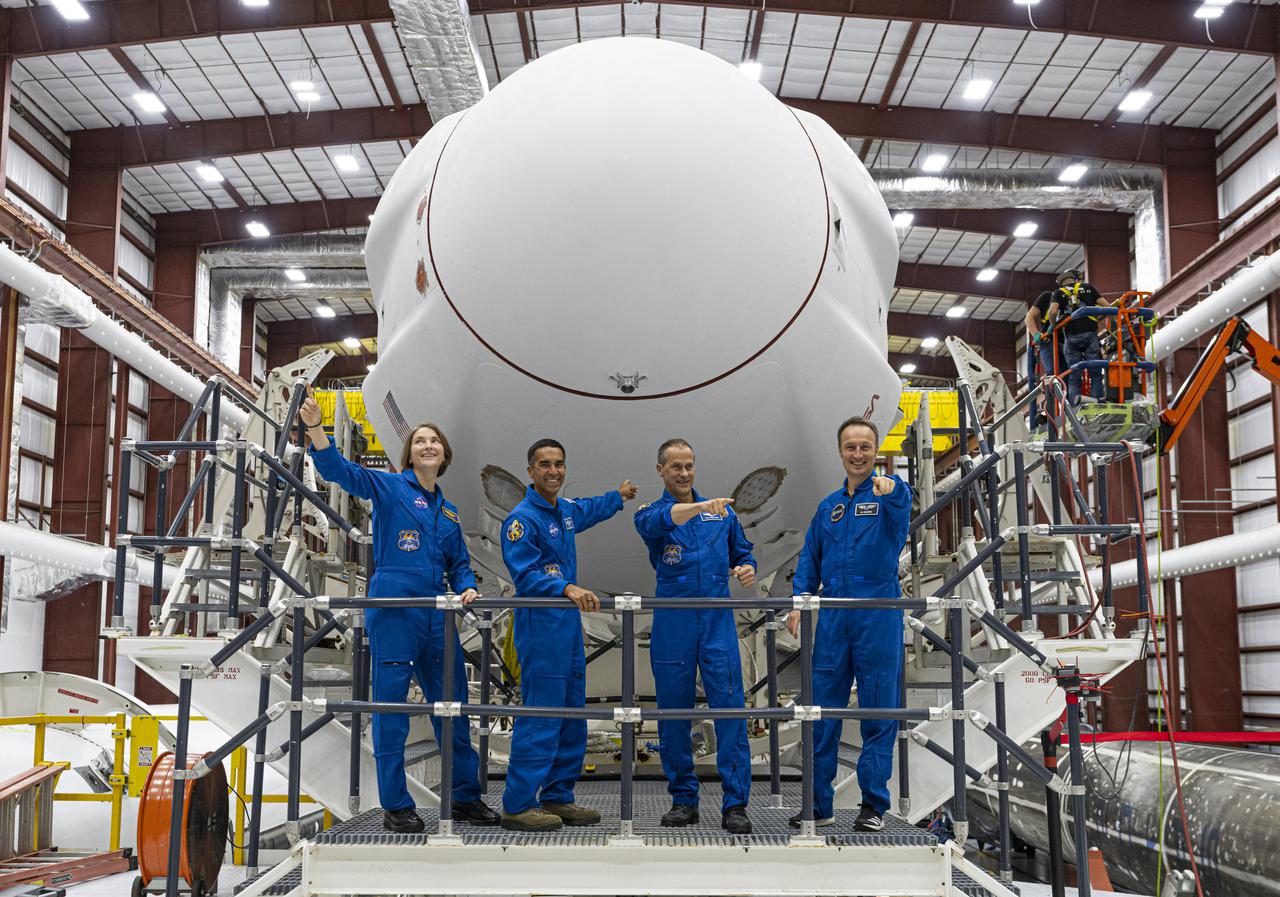 The SpaceX Crew-3 astronauts stand on the transporter in front of the Crew Dragon and Falcon 9 stack inside the SpaceX horizontal processing facility near Launch Complex 39A at Kennedy Space Center in Florida on Oct. 26, 2021. From left are NASA astronauts Kayla Barron, Raja Chari, and Tom Marshburn, along with Matthias Maurer with the European Space Agency. The four-person crew will launch aboard the Crew Dragon atop the Falcon 9 on Oct. 31 to the International Space Station. Launch is targeted for 2:21 a.m. EDT from Pad 39A. Crew-3 is the third crew rotation flight to the space station for NASA’s Commercial Crew Program, and the first flight of a new Crew Dragon spacecraft.
