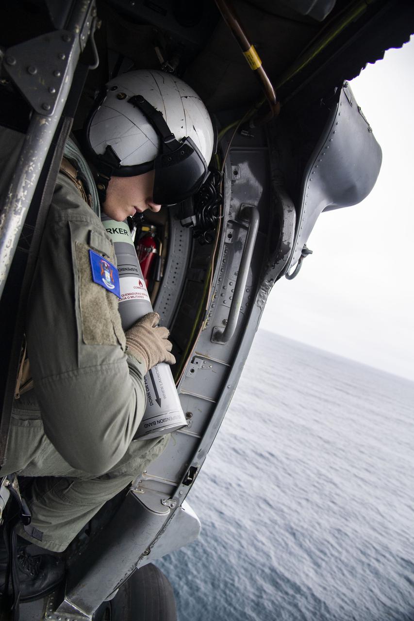 Naval Aircrewman 2nd Class Kanon Brooks, assigned to the “Wild Cards” of Helicopter Sea Combat Squadron (HSC) 23, prepares to drop a smoke canister from an MH-60S Seahawk helicopter near a mock Orion capsule to indicate the spacecraft’s location. During Underway Recovery Test 9 (URT-9) aboard amphibious transport dock ship USS John P. Murtha (LPD 26), NASA’s Landing and Recovery Team conducted a full mission profile simulation to certify the team for Artemis I.