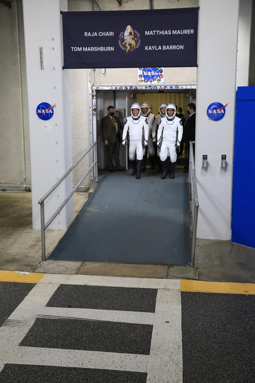 The SpaceX Crew-3 astronauts walk out through the double doors below the Neil A. Armstrong Building’s Astronaut Crew Quarters at NASA’s Kennedy Space Center in Florida on Nov. 10, 2021. They will make their way to the customized Tesla Model X cars that will take them to their spacecraft at Launch Complex 39A. In front, from left, are NASA astronauts Tom Marshburn, pilot, and Raja Chari, commander. Behind them, from left, are Matthias Maurer, ESA (European Space Agency astronaut) and mission specialist; and NASA astronaut Kayla Barron, mission specialist. The Falcon 9 rocket with Crew Dragon Endurance will launch the four-person crew to the International Space Station for NASA’s Commercial Crew Program. Crew-3 is scheduled to launch at 9:03 p.m. EST from Launch Complex 39A at Kennedy.