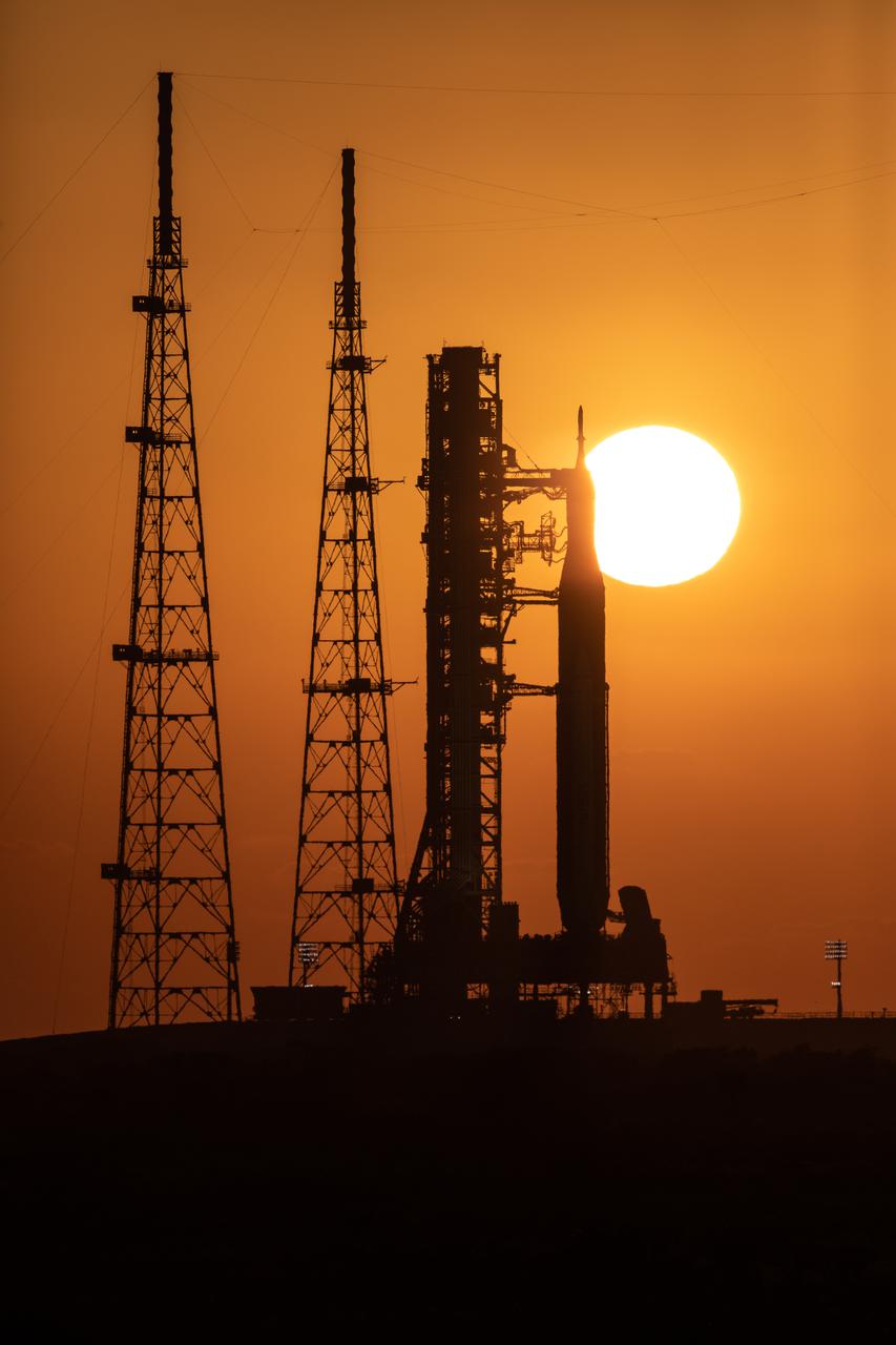A sunrise view of the Artemis I Space Launch System (SLS) and Orion spacecraft at Launch Pad 39B at NASA’s Kennedy Space Center in Florida on March 21, 2022. The SLS and Orion atop the mobile launcher were transported to the pad on crawler-transporter 2 for a prelaunch test called a wet dress rehearsal. Artemis I will be the first integrated test of the SLS and Orion spacecraft. In later missions, NASA will land the first woman and the first person of color on the surface of the Moon, paving the way for a long-term lunar presence and serving as a steppingstone on the way to Mars. 
