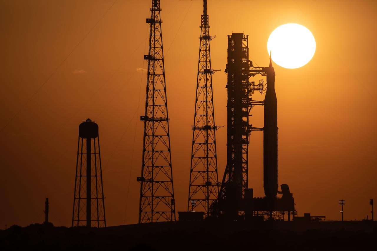 A sunrise view of the Artemis I Space Launch System (SLS) and Orion spacecraft at Launch Pad 39B at NASA’s Kennedy Space Center in Florida on March 21, 2022. The SLS and Orion atop the mobile launcher were transported to the pad on crawler-transporter 2 for a prelaunch test called a wet dress rehearsal. Artemis I will be the first integrated test of the SLS and Orion spacecraft. In later missions, NASA will land the first woman and the first person of color on the surface of the Moon, paving the way for a long-term lunar presence and serving as a steppingstone on the way to Mars. 