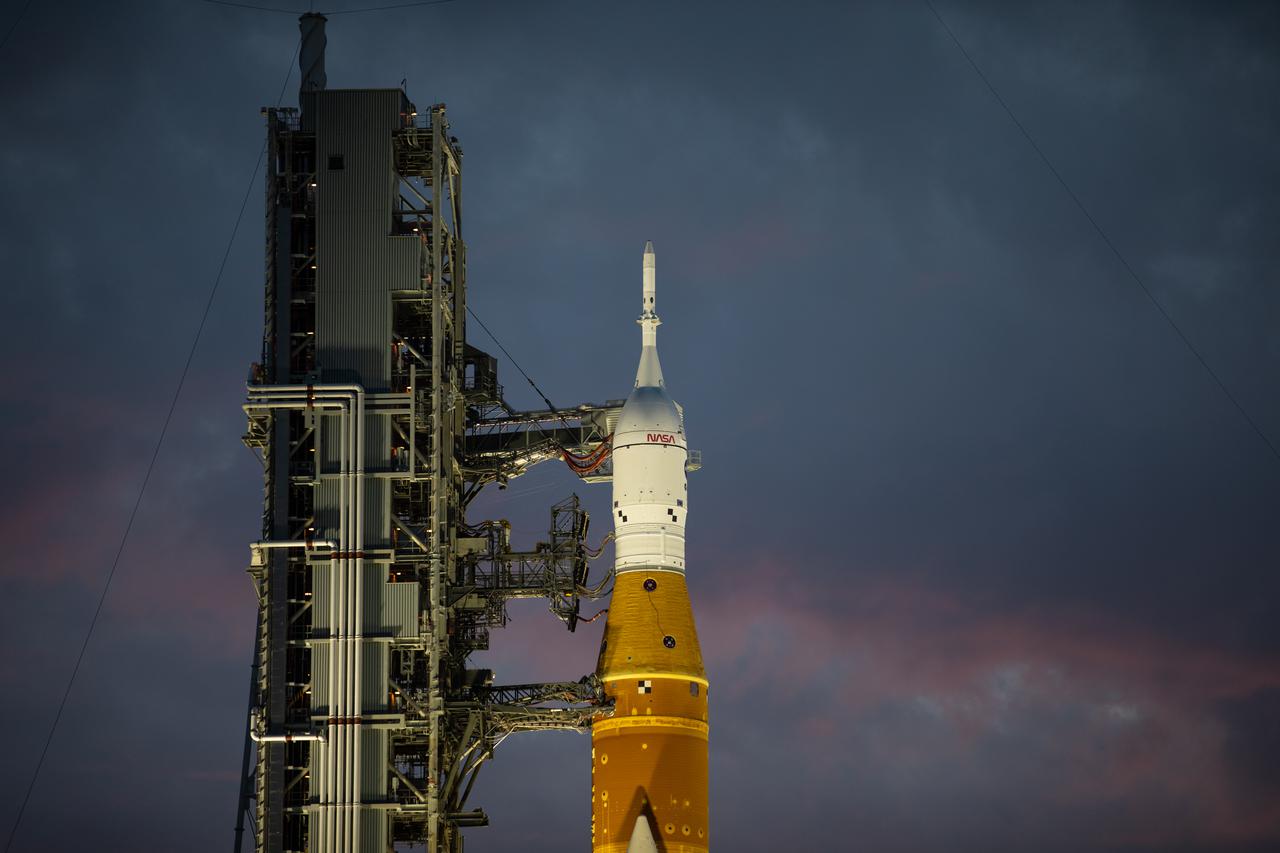 A view of the Artemis I Space Launch System (SLS) and Orion spacecraft just before sunrise at Launch Pad 39B at NASA’s Kennedy Space Center in Florida on March 23, 2022. The SLS and Orion atop the mobile launcher were transported to the pad on crawler-transporter 2 for a prelaunch test called a wet dress rehearsal. Artemis I will be the first integrated test of the SLS and Orion spacecraft. In later missions, NASA will land the first woman and the first person of color on the surface of the Moon, paving the way for a long-term lunar presence and serving as a steppingstone on the way to Mars