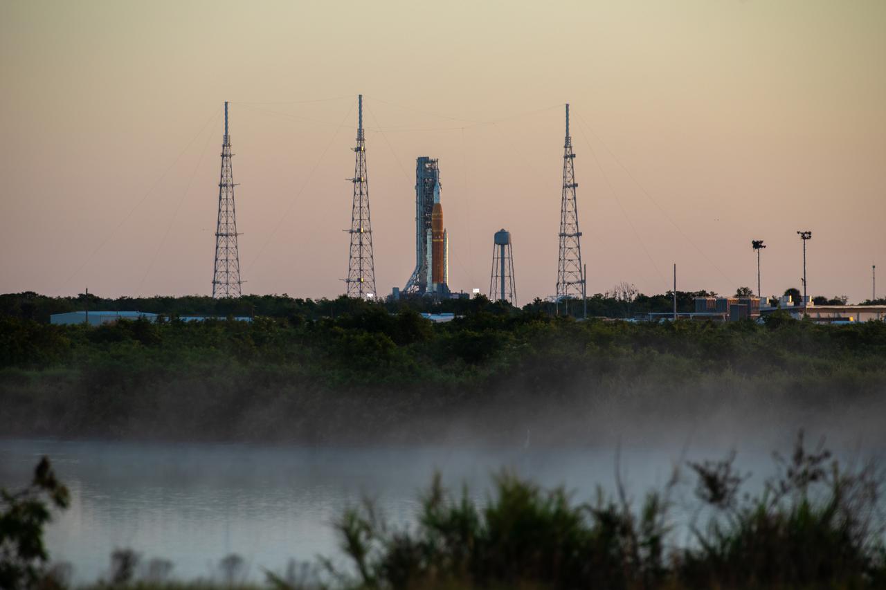 A sunrise view of the Artemis I Space Launch System (SLS) and Orion spacecraft at Launch Pad 39B at NASA’s Kennedy Space Center in Florida on April 11, 2022. Mist rises from a nearby waterway. The SLS and Orion atop the mobile launcher were transported to the pad on crawler-transporter 2 for a prelaunch test called a wet dress rehearsal. Artemis I will be the first integrated test of the SLS and Orion spacecraft. In later missions, NASA will land the first woman and the first person of color on the surface of the Moon, paving the way for a long-term lunar presence and serving as a steppingstone on the way to Mars. 