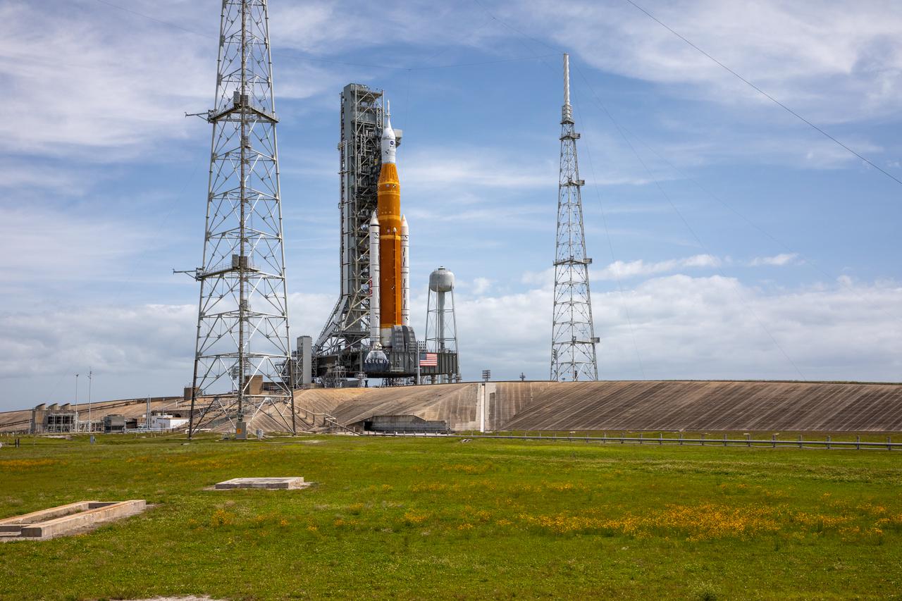 A view of the Artemis I Space Launch System (SLS) and Orion spacecraft on Launch Pad 39B at NASA’s Kennedy Space Center in Florida on April 21, 2022. Also in view are two of the three lightning protection towers and the water tower. The SLS and Orion atop the mobile launcher were transported to the pad on crawler-transporter 2 for a prelaunch test called a wet dress rehearsal. Artemis I will be the first integrated test of the SLS and Orion spacecraft. In future Artemis missions, NASA will land the first woman and the first person of color on the surface of the Moon, paving the way for a long-term lunar presence and serving as a steppingstone on the way to Mars.