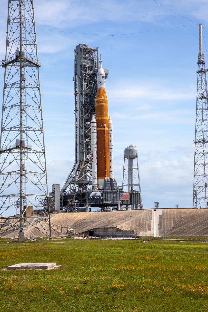 A view of the Artemis I Space Launch System (SLS) and Orion spacecraft on Launch Pad 39B at NASA’s Kennedy Space Center in Florida on April 21, 2022. Also in view are two of the three lightning protection towers and the water tower. The SLS and Orion atop the mobile launcher were transported to the pad on crawler-transporter 2 for a prelaunch test called a wet dress rehearsal. Artemis I will be the first integrated test of the SLS and Orion spacecraft. In future Artemis missions, NASA will land the first woman and the first person of color on the surface of the Moon, paving the way for a long-term lunar presence and serving as a steppingstone on the way to Mars.