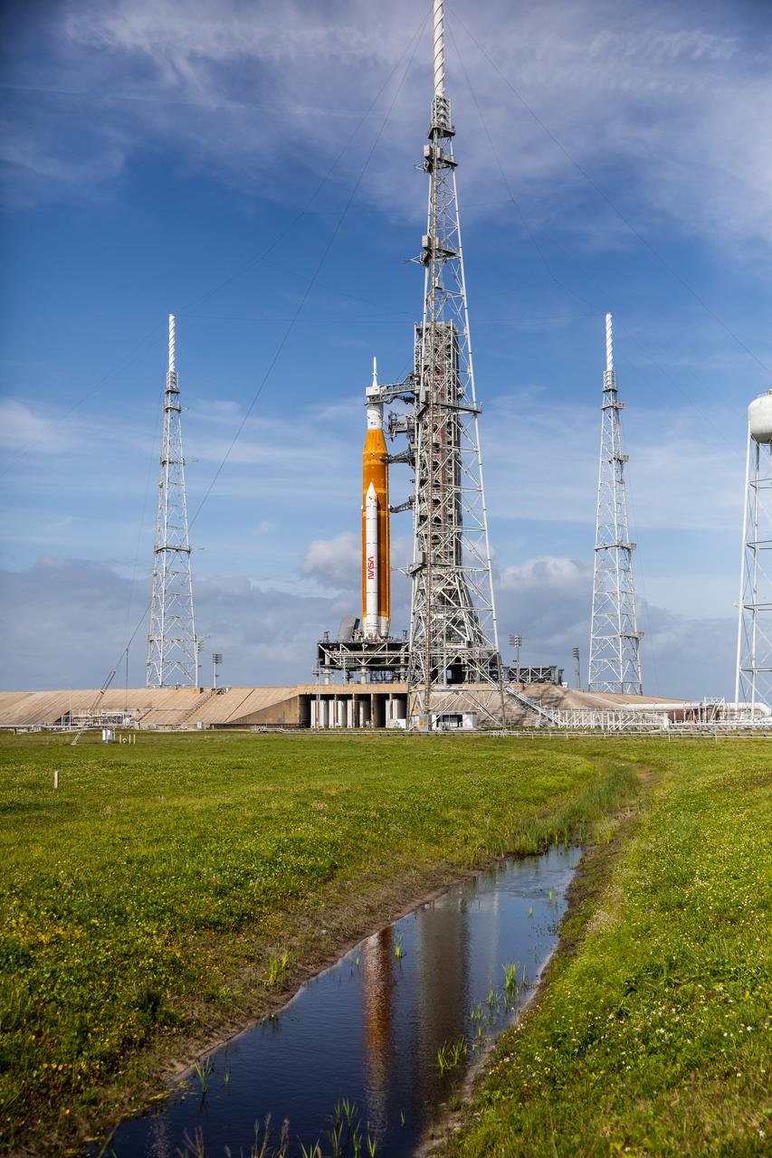 A view of the Artemis I Space Launch System (SLS) and Orion spacecraft atop the mobile launcher on Launch Pad 39B at NASA’s Kennedy Space Center in Florida on April 21, 2022. Also in view are the three lightning protection towers and water tower. The SLS and Orion atop the mobile launcher were transported to the pad on crawler-transporter 2 for a prelaunch test called a wet dress rehearsal. Artemis I will be the first integrated test of the SLS and Orion spacecraft. In future Artemis missions, NASA will land the first woman and the first person of color on the surface of the Moon, paving the way for a long-term lunar presence and serving as a steppingstone on the way to Mars.