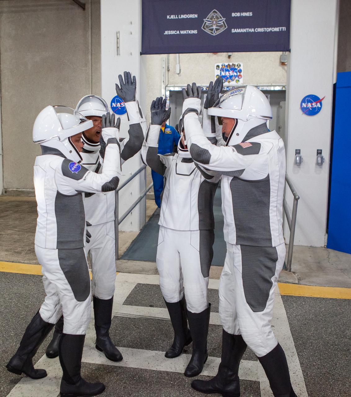 Crew-4 astronauts Jessica Watkins, Bob Hines, Samantha Cristoforetti, and Kjell Lindgren form a huddle after walking out through the double doors below the Neil A. Armstrong Building’s Astronaut Crew Quarters at NASA’s Kennedy Space Center in Florida on April 27, 2022. They are making their way to the customized Tesla Model X vehicles that will take them to their spacecraft at Launch Complex 39A. SpaceX’s Crew Dragon, powered by the company’s Falcon 9 rocket, will carry the four-person crew to the International Space Station as part of NASA’s Commercial Crew Program. Crew-4 is scheduled to launch today at 3:52 a.m. EDT, from Pad 39A at Kennedy.