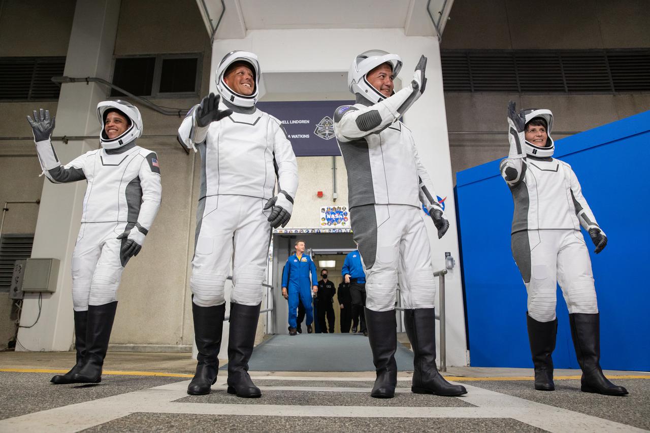 Crew-4 astronauts wave after walking out through the double doors below the Neil A. Armstrong Building’s Astronaut Crew Quarters at NASA’s Kennedy Space Center in Florida on April 27, 2022. They will make their way to the customized Tesla Model X cars that will take them to their spacecraft at Launch Complex 39A. From left are: mission specialist Jessica Watkins, pilot Bob Hines, commander Kjell Lindgren, and mission specialist Samantha Cristoforetti. SpaceX’s Crew Dragon, powered by the company’s Falcon 9 rocket, will carry the four-person crew to the International Space Station as part of NASA’s Commercial Crew Program. Crew-4 is scheduled to launch today at 3:52 a.m. EDT, from Pad 39A at Kennedy.