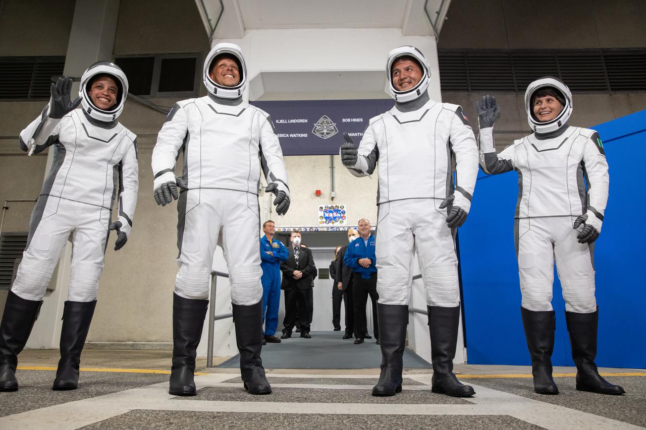 Crew-4 astronauts wave after walking out through the double doors below the Neil A. Armstrong Building’s Astronaut Crew Quarters at NASA’s Kennedy Space Center in Florida on April 27, 2022. They will make their way to the customized Tesla Model X cars that will take them to their spacecraft at Launch Complex 39A. From left are: mission specialist Jessica Watkins, pilot Bob Hines, commander Kjell Lindgren, and mission specialist Samantha Cristoforetti. SpaceX’s Crew Dragon, powered by the company’s Falcon 9 rocket, will carry the four-person crew to the International Space Station as part of NASA’s Commercial Crew Program. Crew-4 is scheduled to launch today at 3:52 a.m. EDT, from Pad 39A at Kennedy.