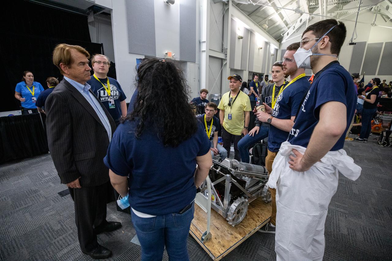 Thad Altman, far left, chairman and CEO of the Astronaut Memorial Foundation, talks to students from the University of New Hampshire as they prepare to take their robotic miner for its turn to dig in the mining arena during NASA’s LUNABOTICS competition on May 26, 2022, at the Center for Space Education near the Kennedy Space Center Visitor Complex in Florida. More than 35 teams from around the U.S. have designed and built remote-controlled robots for the mining competition. Teams use their semi-autonomous or remote-controlled robots to maneuver and dig in a supersized sandbox filled with rocks and simulated lunar soil, or regolith. The objective of the challenge is to see which team’s robot can collect and deposit the most rocky regolith within a specified amount of time. 