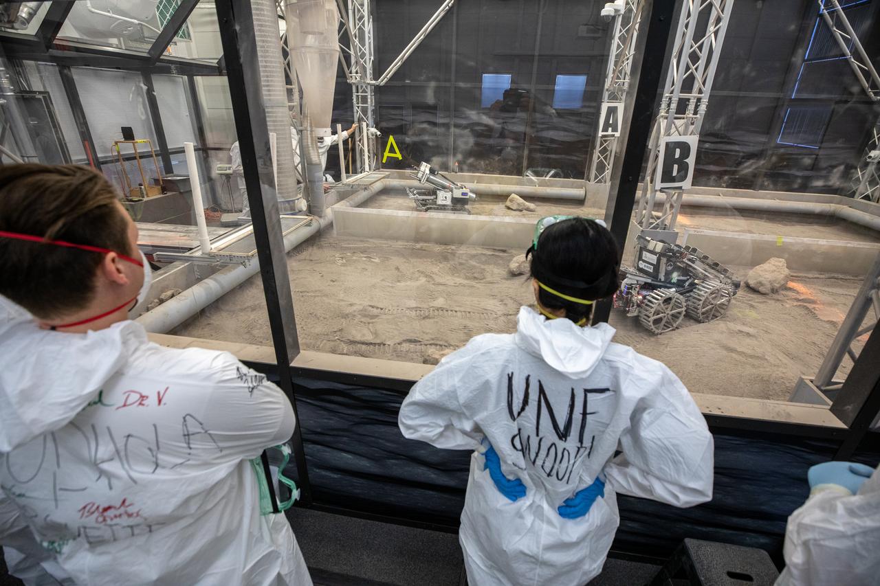 Team members from the University of North Florida watch their robotic miner dig in the mining arena  NASA’s LUNABOTICS competition on May 27, 2022, at the Center for Space Education near the Kennedy Space Center Visitor Complex in Florida. More than 35 teams from around the U.S. have designed and built remote-controlled robots for the mining competition. Teams used their autonomous or remote-controlled robots to maneuver and dig in a supersized sandbox filled with lunar simulant and rocks. The objective of the challenge is to see which team’s robot can collect and deposit the most rocky regolith within a specified amount of time. 