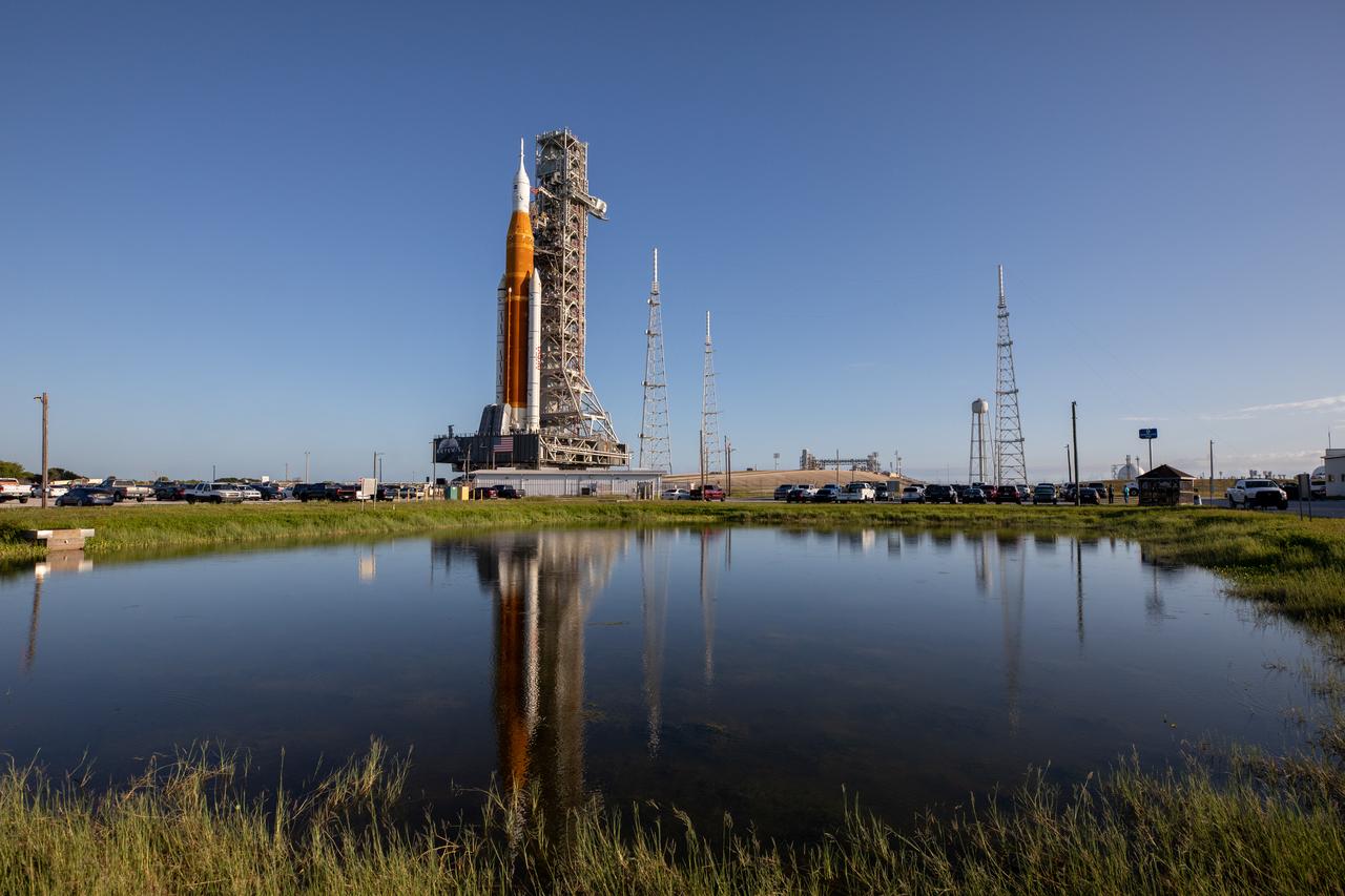 NASA’s Artemis I Moon rocket – carried atop the crawler-transporter 2 – is reflected in the water as it approaches Launch Pad 39B at the agency’s Kennedy Space Center in Florida on June 6, 2022. The rocket rolled out of the Vehicle Assembly Building in the early morning hours to travel the 4.2 miles to the launch pad for NASA’s next wet dress rehearsal attempt ahead of the Artemis I launch. The first in an increasingly complex series of missions, Artemis I will test the Space Launch System rocket and Orion spacecraft as an integrated system prior to crewed flights to the Moon. Through Artemis, NASA will land the first woman and first person of color on the lunar surface, paving the way for a long-term lunar presence and using the Moon as a steppingstone before venturing to Mars.