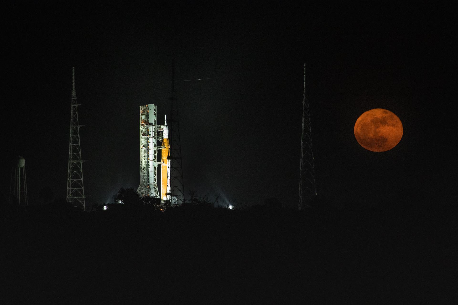 A full Moon is in view from Launch Complex 39B at NASA’s Kennedy Space Center in Florida on June 14, 2022. The Artemis I Space Launch System (SLS) and Orion spacecraft, atop the mobile launcher, are being prepared for a wet dress rehearsal to practice timelines and procedures for launch. The first in an increasingly complex series of missions, Artemis I will test SLS and Orion as an integrated system prior to crewed flights to the Moon. Through Artemis, NASA will land the first woman and first person of color on the lunar surface, paving the way for a long-term lunar presence and using the Moon as a steppingstone on the way to Mars.