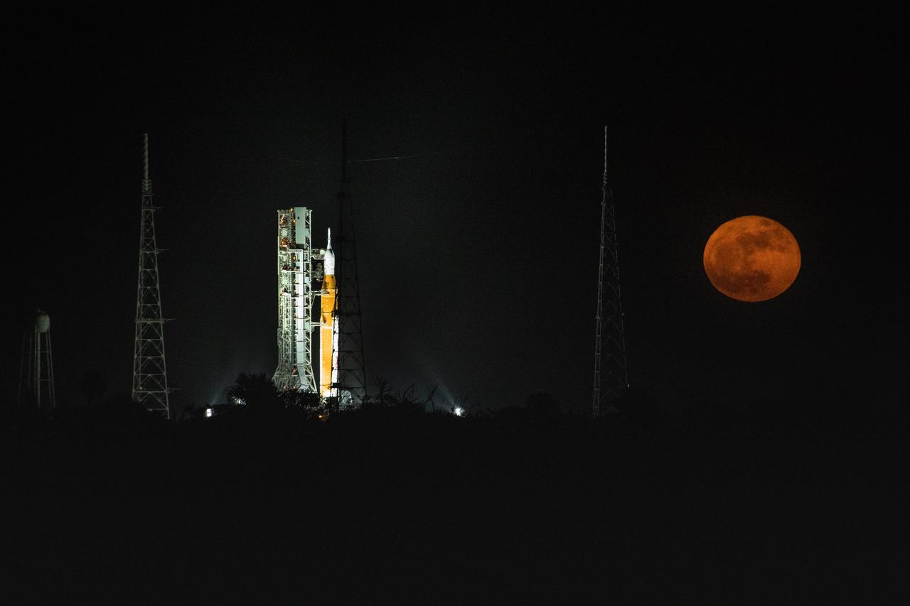 A full Moon is in view from Launch Complex 39B at NASA’s Kennedy Space Center in Florida on June 14, 2022. The Artemis I Space Launch System (SLS) and Orion spacecraft, atop the mobile launcher, are being prepared for a wet dress rehearsal to practice timelines and procedures for launch. The first in an increasingly complex series of missions, Artemis I will test SLS and Orion as an integrated system prior to crewed flights to the Moon. Through Artemis, NASA will land the first woman and first person of color on the lunar surface, paving the way for a long-term lunar presence and using the Moon as a steppingstone on the way to Mars.