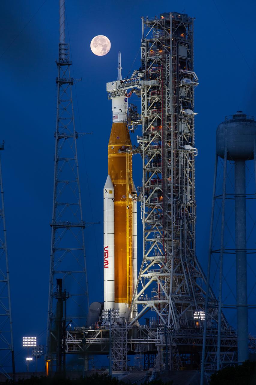 A full Moon is in view from Launch Complex 39B at NASA’s Kennedy Space Center in Florida on June 14, 2022. The Artemis I Space Launch System (SLS) and Orion spacecraft, atop the mobile launcher, are being prepared for a wet dress rehearsal to practice timelines and procedures for launch. The first in an increasingly complex series of missions, Artemis I will test SLS and Orion as an integrated system prior to crewed flights to the Moon. Through Artemis, NASA will land the first woman and first person of color on the lunar surface, paving the way for a long-term lunar presence and using the Moon as a steppingstone on the way to Mars.