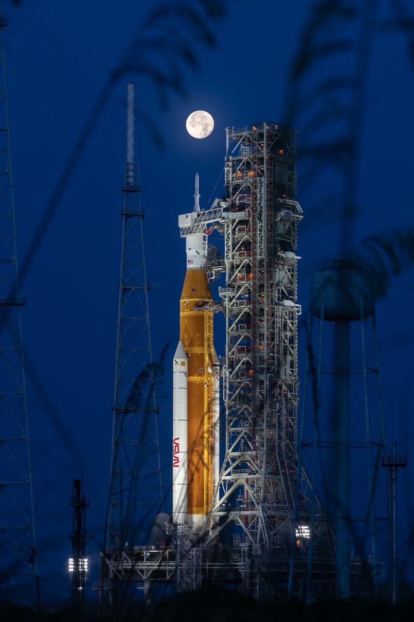 A full Moon is in view from Launch Complex 39B at NASA’s Kennedy Space Center in Florida on June 14, 2022. The Artemis I Space Launch System (SLS) and Orion spacecraft, atop the mobile launcher, are being prepared for a wet dress rehearsal to practice timelines and procedures for launch. The first in an increasingly complex series of missions, Artemis I will test SLS and Orion as an integrated system prior to crewed flights to the Moon. Through Artemis, NASA will land the first woman and first person of color on the lunar surface, paving the way for a long-term lunar presence and using the Moon as a steppingstone on the way to Mars.