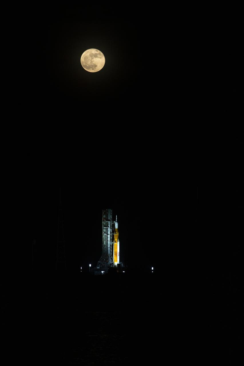 A full Moon is in view from Launch Complex 39B at NASA’s Kennedy Space Center in Florida on June 14, 2022. The Artemis I Space Launch System (SLS) and Orion spacecraft, atop the mobile launcher, are being prepared for a wet dress rehearsal to practice timelines and procedures for launch. The first in an increasingly complex series of missions, Artemis I will test SLS and Orion as an integrated system prior to crewed flights to the Moon. Through Artemis, NASA will land the first woman and first person of color on the lunar surface, paving the way for a long-term lunar presence and using the Moon as a steppingstone on the way to Mars.