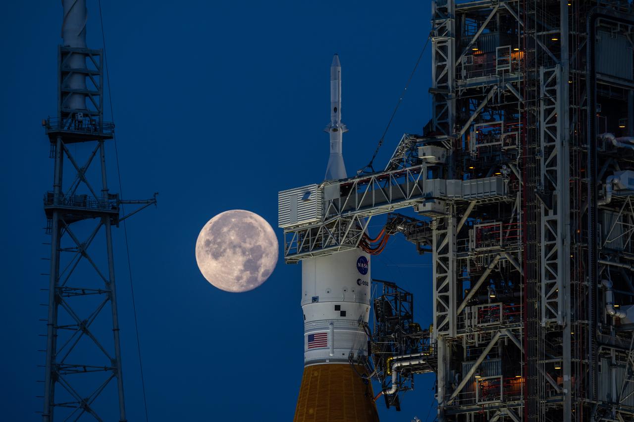 A full Moon is in view from Launch Complex 39B at NASA’s Kennedy Space Center in Florida on June 14, 2022. The Artemis I Space Launch System (SLS) and Orion spacecraft, atop the mobile launcher, are being prepared for a wet dress rehearsal to practice timelines and procedures for launch. The first in an increasingly complex series of missions, Artemis I will test SLS and Orion as an integrated system prior to crewed flights to the Moon. Through Artemis, NASA will land the first woman and first person of color on the lunar surface, paving the way for a long-term lunar presence and using the Moon as a steppingstone on the way to Mars.