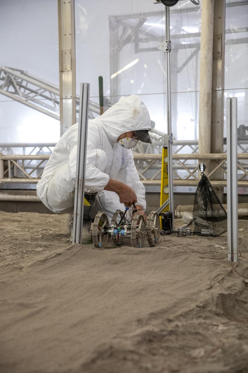 Senior Software Engineer Taylor Whitaker stages Astrobotic’s mass-offloaded CubeRover – a lightweight, modular planetary rover – for a drawbar pull test inside the Granular Mechanics and Regolith Operations (GMRO) Laboratory’s regolith pit at NASA Kennedy Space Center’s Swamp Works facility on June 30, 2022. Astrobotic – a Pittsburgh-based space robotics company – is using the GMRO lab’s regolith bin, which holds approximately 120 tons of lunar regolith simulant, to depict how the company’s CubeRover would perform on the Moon. NASA’s Small Business Innovation Research program provided the funding for initial development, and a $2 million Tipping Point award from the agency has provided additional funding for continued development into a more mature rover.
