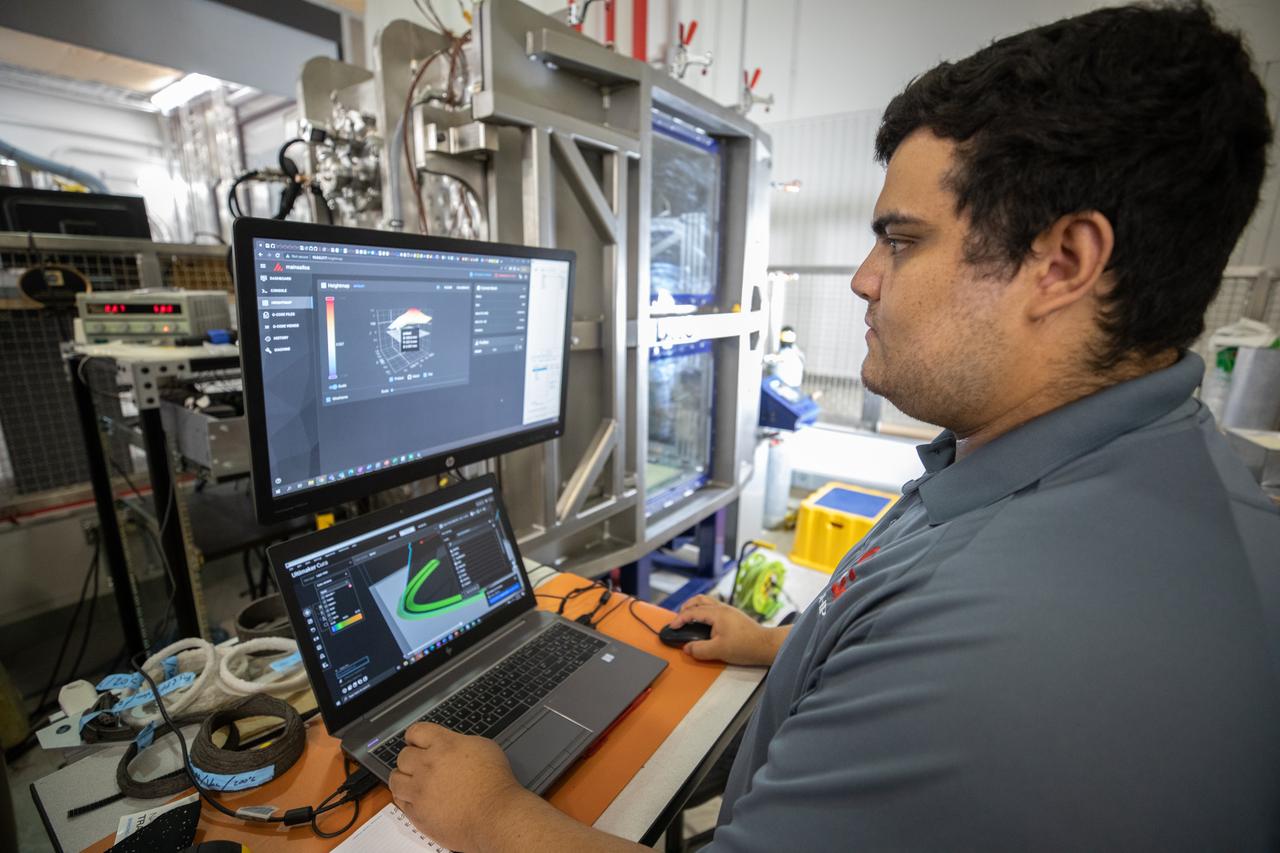 NASA Internships, Fellowships, and Scholarships (NIFS) intern Leonel Herrera tests a 3D printer on July 28, 2022, at Swamp Works at NASA’s Kennedy Space Center in Florida, as part of the Relevant Environment Additive Construction Technology (REACT) project. Among the key objectives of the project is developing an architectural and structural design for a shelter that provides protection to habitable assets on the lunar surface. Testing REACT derives from NASA’s 2020 Announcement of Collaboration Opportunity with AI SpaceFactory – an architectural and construction technology company and winner of NASA’s 3D Printed Habitat Challenge.