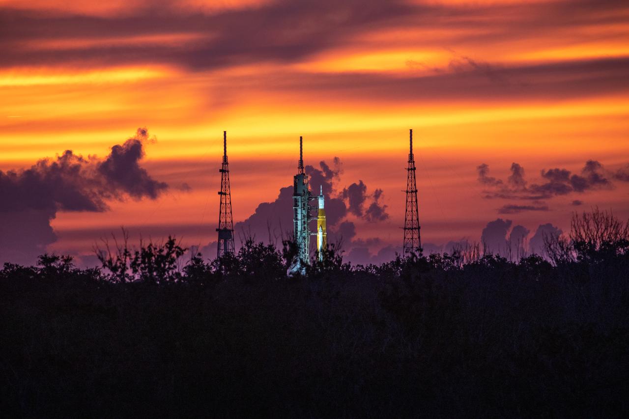 A golden sunrise surrounds NASA’s Space Launch System and Orion spacecraft for Artemis I on the pad at Launch Complex 39B at NASA’s Kennedy Space Center in Florida on Aug. 22, 2022. Launch of Artemis I is scheduled for no earlier than Aug. 29, 2022, at 8:33 a.m. EDT. The first in a series of increasingly complex missions, Artemis I will provide a foundation for human deep space exploration and demonstrate our commitment and capability to extend human presence to the Moon and beyond. The primary goal of Artemis I is to thoroughly test the integrated systems before crewed missions by operating the spacecraft in a deep space environment, testing Orion’s heat shield, and recovering the crew module after reentry, descent, and splashdown. 