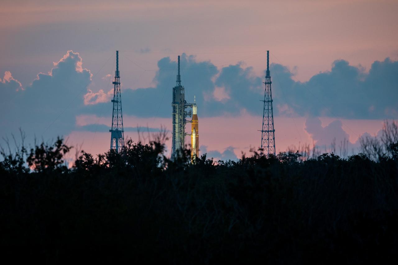 A sunrise view of NASA’s Space Launch System and Orion spacecraft for Artemis I on the pad at Launch Complex 39B at NASA’s Kennedy Space Center in Florida on Aug. 22, 2022. Launch of Artemis I is scheduled for no earlier than Aug. 29, 2022, at 8:33 a.m. EDT. The first in a series of increasingly complex missions, Artemis I will provide a foundation for human deep space exploration and demonstrate our commitment and capability to extend human presence to the Moon and beyond. The primary goal of Artemis I is to thoroughly test the integrated systems before crewed missions by operating the spacecraft in a deep space environment, testing Orion’s heat shield, and recovering the crew module after reentry, descent, and splashdown. 