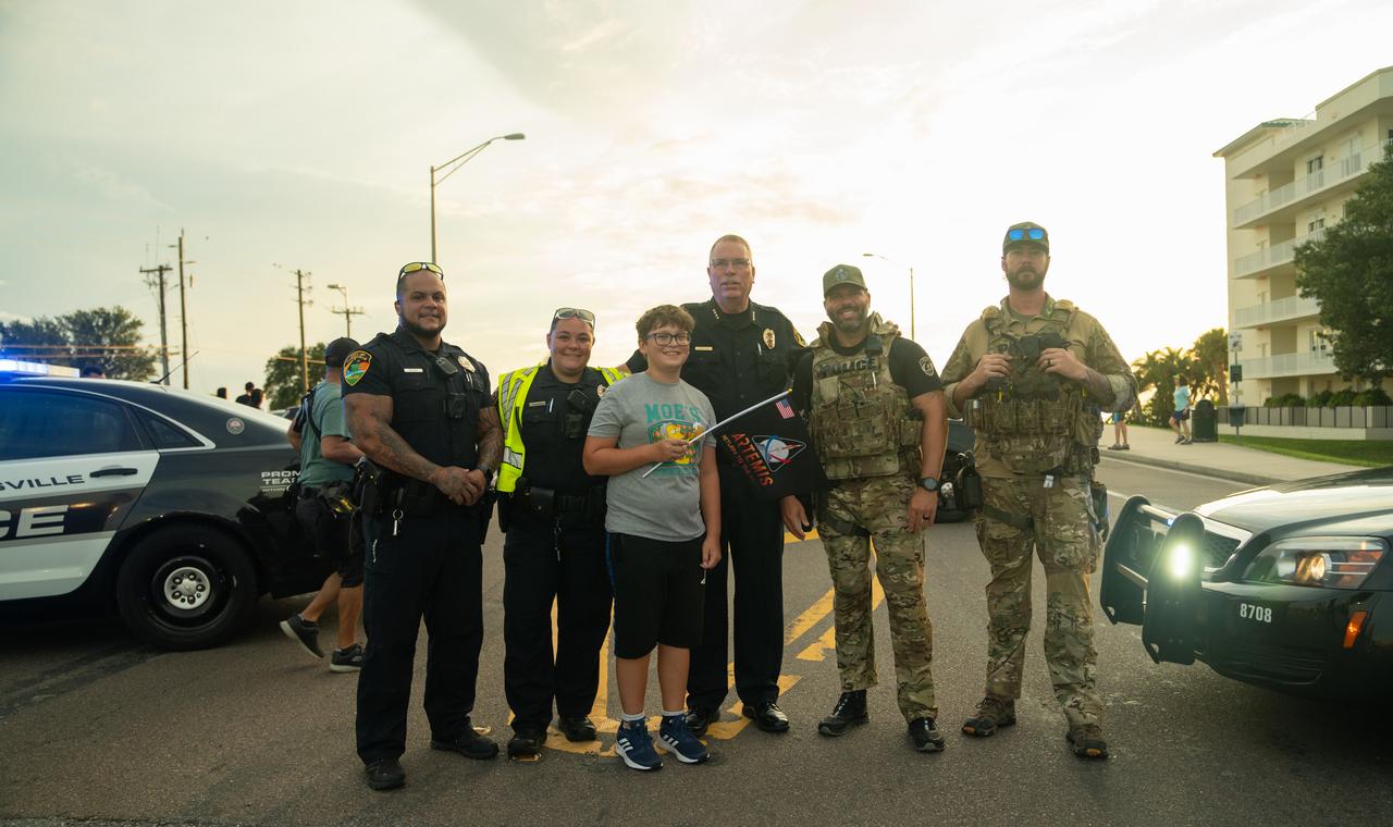 A young child waving an Artemis flag poses with members of the Titusville Police Dept. on the Max Brewer Bridge on Aug. 29, 2022, during Artemis I countdown festivities. The launch was waved off for the day at the agency’s Kennedy Space Center. The first in a series of increasingly complex missions, Artemis I will provide a foundation for human deep space exploration and demonstrate our commitment and capability to extend human presence to the Moon and beyond. The primary goal of Artemis I is to thoroughly test the integrated systems before crewed missions by operating the spacecraft in a deep space environment, testing Orion’s heat shield, and recovering the crew module after reentry, descent, and splashdown. 