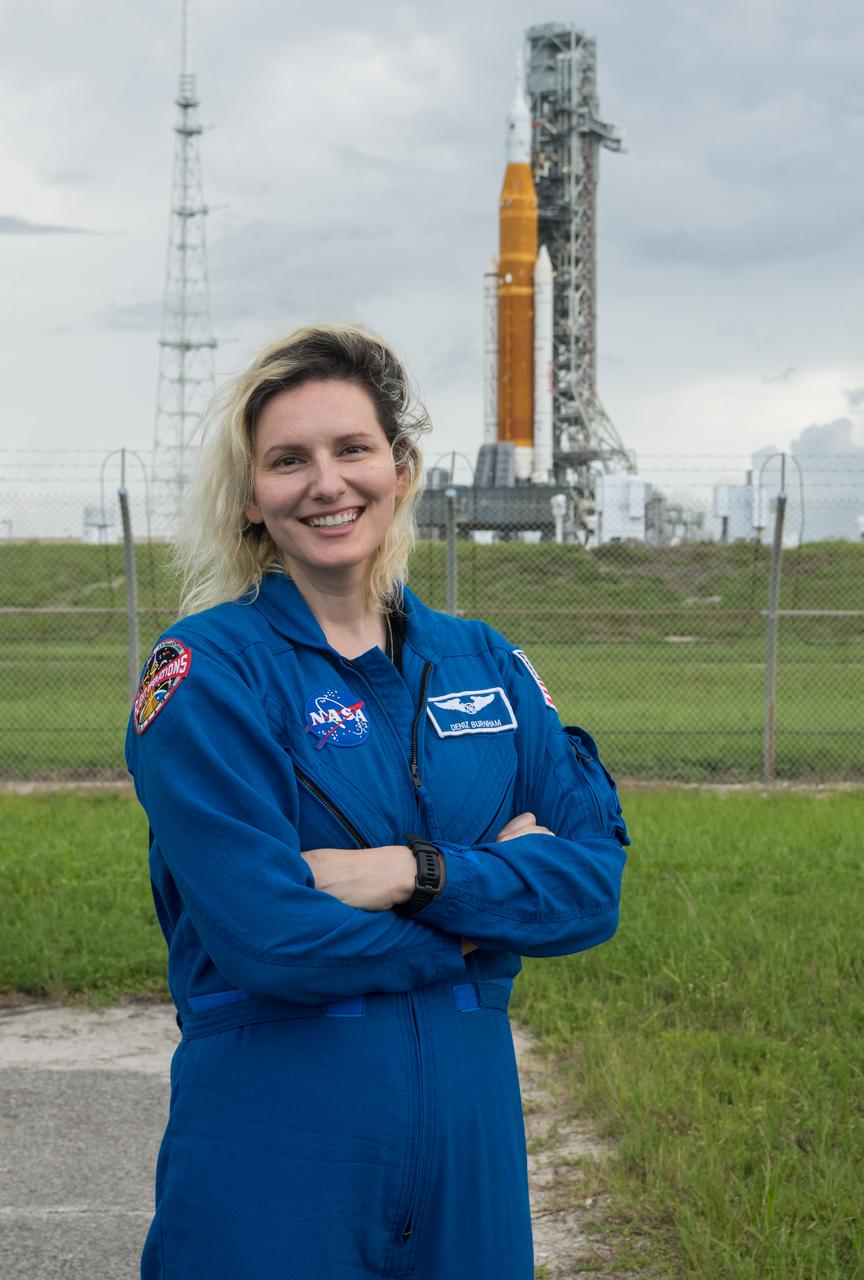 NASA astronaut candidate Deniz Burnham poses for a photograph in front of NASA’s Artemis I Space Launch System and Orion spacecraft atop the mobile launcher on the pad at Launch Complex 39B at the agency’s Kennedy Space Center in Florida on Sept. 2, 2022. The first in a series of increasingly complex missions, Artemis I will provide a foundation for human deep space exploration and demonstrate our commitment and capability to extend human presence to the Moon and beyond. The primary goal of Artemis I is to thoroughly test the integrated systems before crewed missions by operating the spacecraft in a deep space environment, testing Orion’s heat shield, and recovering the crew module after reentry, descent, and splashdown. In later missions, NASA will land the first woman and the first person of color on the surface of the Moon, paving the way for a long-term lunar presence and serving as a steppingstone on the way to Mars.