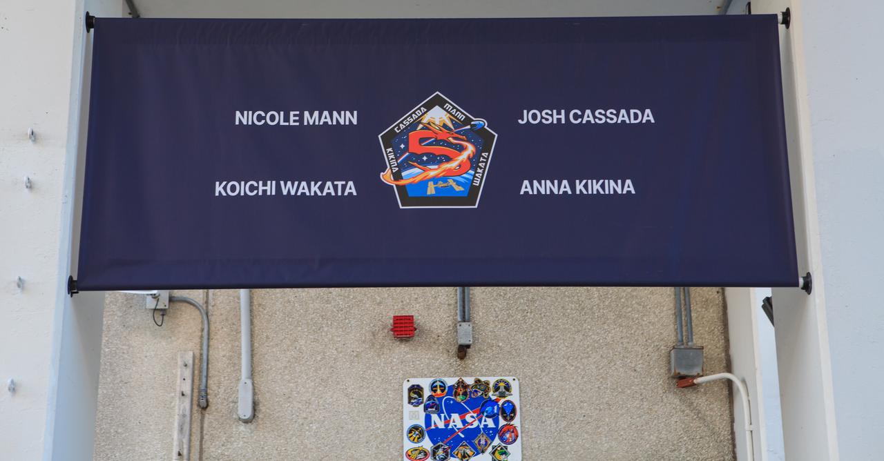 A banner displaying NASA’s SpaceX Crew-5 mission patch and crew names is photographed above the double doors of the Neil A. Armstrong Operations and Checkout Building at the agency’s Kennedy Space Center in Florida on Oct. 5, 2022. NASA astronauts Nicole Mann, spacecraft commander, and Josh Cassada, pilot; Roscosmos cosmonaut Anna Kikina, mission specialist; and JAXA (Japan Aerospace Exploration Agency) astronaut Koichi Wakata, mission specialist, will launch to the International Space Station for a science expedition mission as part of NASA’s Commercial Crew Program. The SpaceX Falcon 9 rocket and Dragon Endurance spacecraft lifted off at noon EDT.