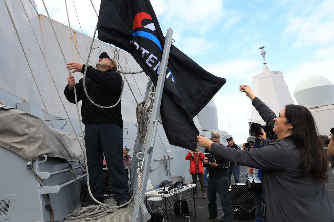 After splashdown of the Orion spacecraft on Dec. 11, 2022, NASA’s Artemis I Landing and Recovery Director Melissa Jones helps to raise the Artemis flag aboard USS Portland.   