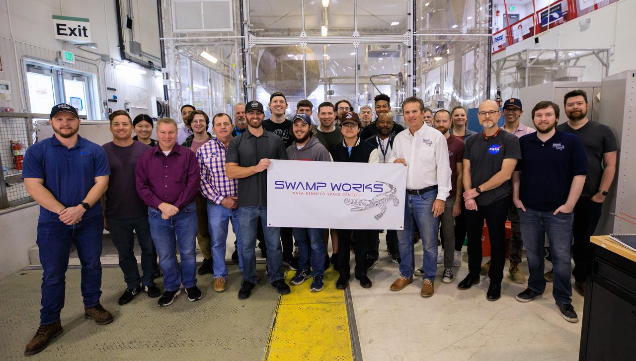 Groups from the Granular Mechanics and Regolith Operations (GMRO) laboratory and the Electrostatics and Surface Physics Laboratory (ESPL) gather for a photograph to celebrate the 10th anniversary of Swamp Works at NASA’s Kennedy Space Center in Florida on Feb. 13, 2023. Studies of the mechanics of materials in a launch pad environment are performed in the GMRO lab. The team also develops technologies for handling lunar and Martian regolith, including excavator technologies, pneumatic transport of soil, and magnetic handling of soil. The ESPL group performs scientific investigations to protect flight hardware and launch equipment from the phenomenon of electrostatic discharges, commonly known as sparks. 
